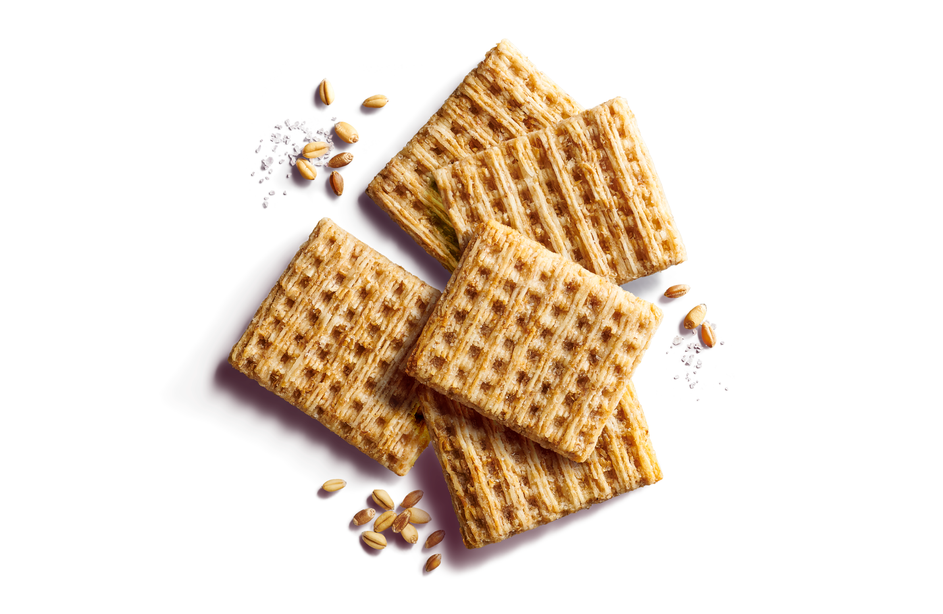 Close-up of five scattered whole grain, woven wheat crackers on a purple background with wheat grains and sea salt flakes.