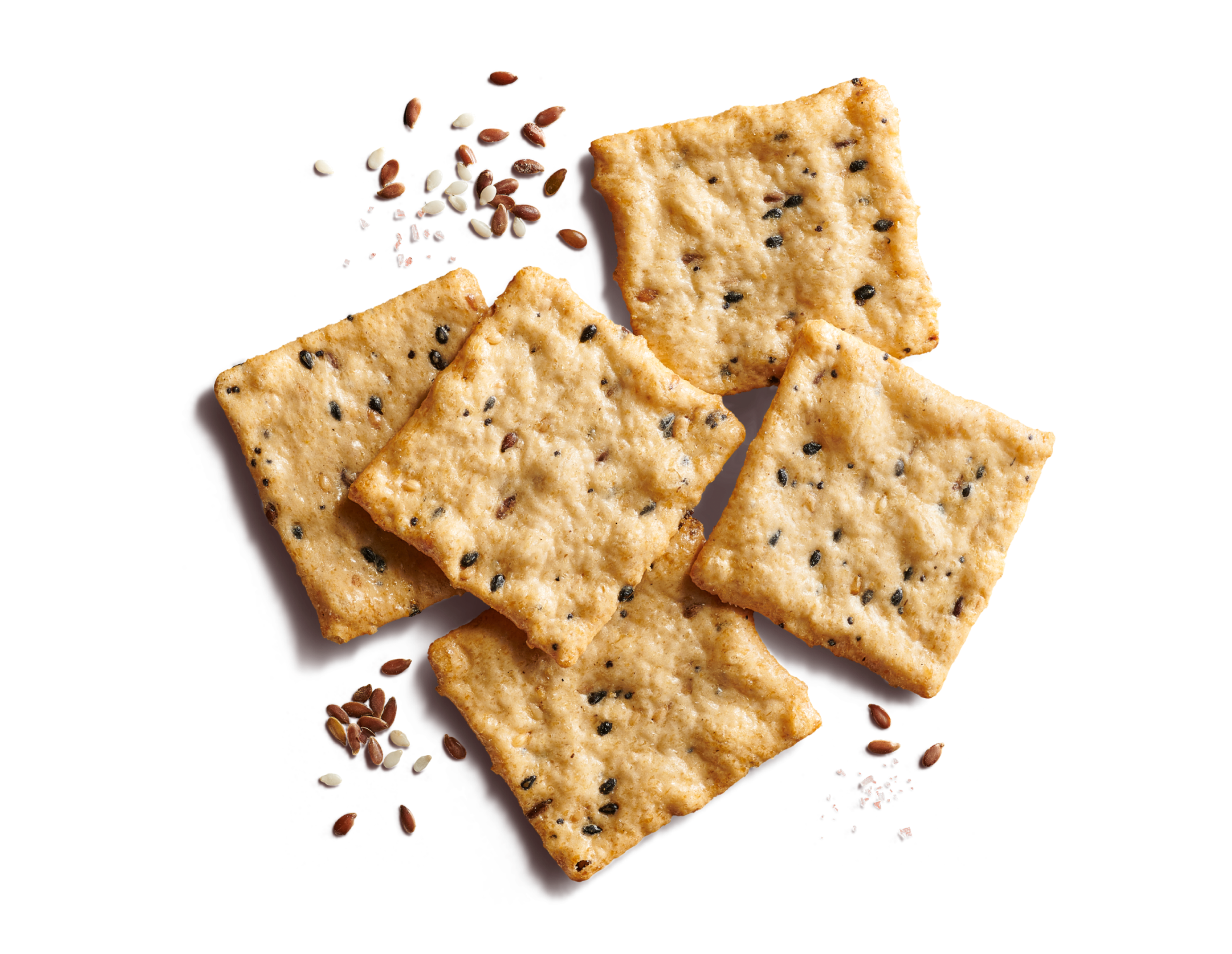 Close-up of five scattered square, multi-seed crackers on a bright orange background with flax seeds, sesame seeds, and sea salt flakes.