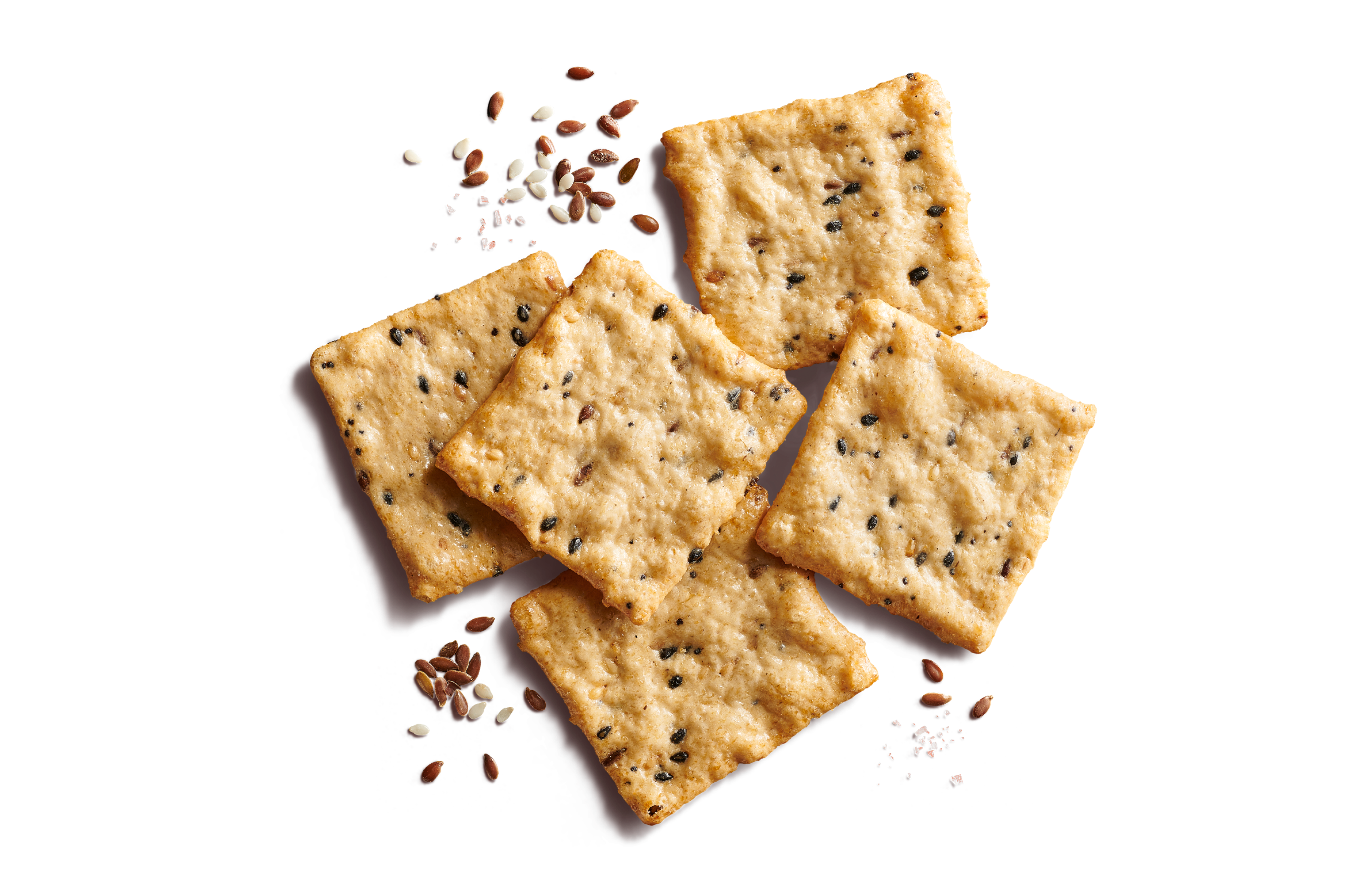 Close-up of five scattered square, multi-seed crackers on a bright orange background with flax seeds, sesame seeds, and sea salt flakes.