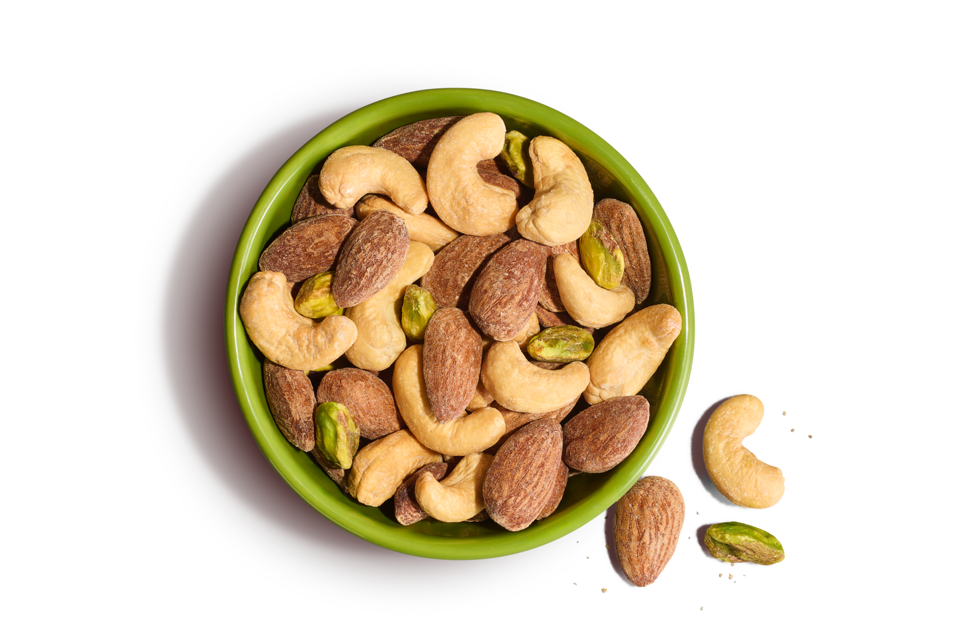 Green bowl of whole cashews, pistachios, and almonds on an orange background.