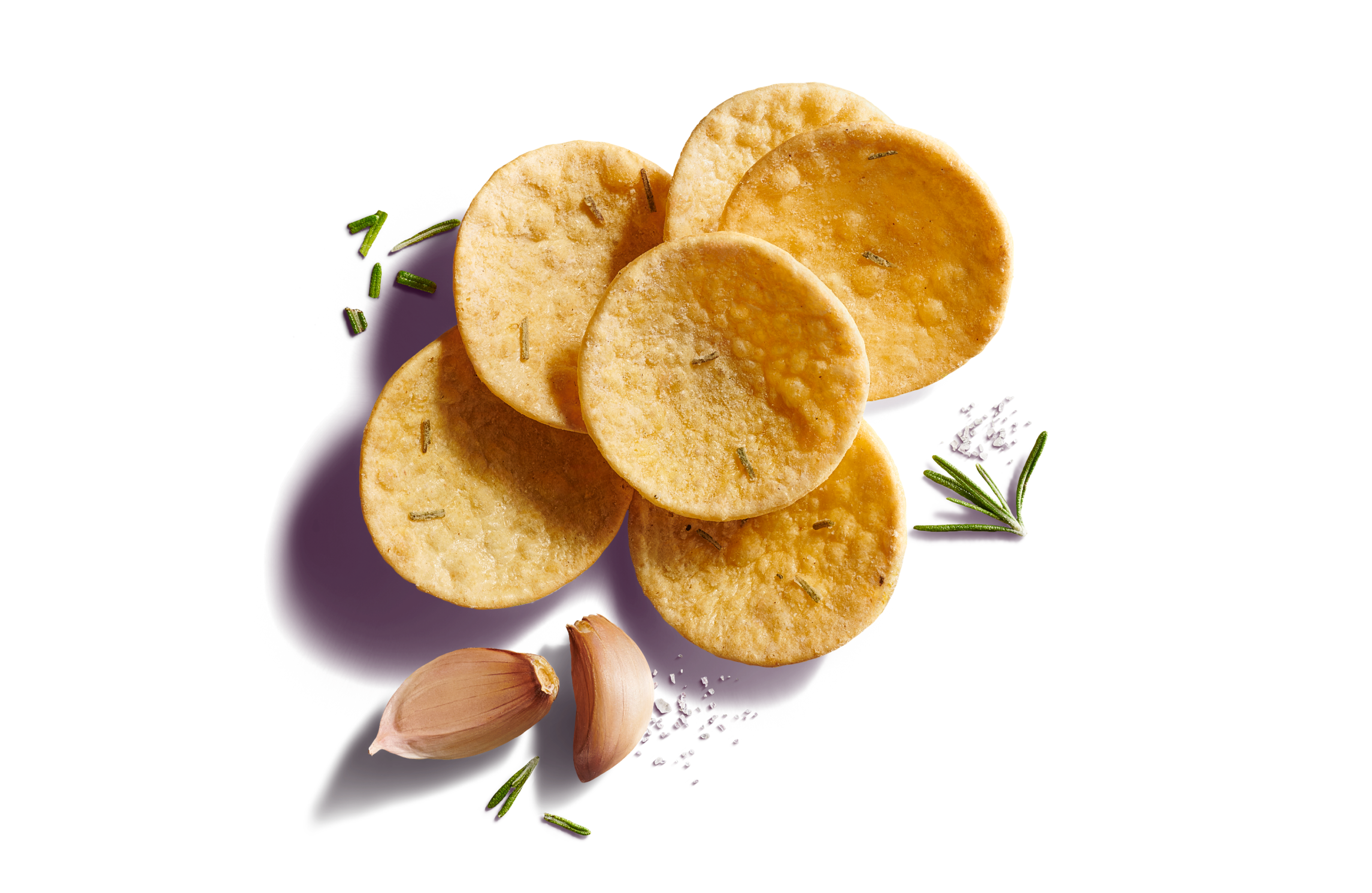 Close-up of six scattered round, curved scoop crackers on a bright purple background with garlic cloves, rosemary, and sea salt flakes.