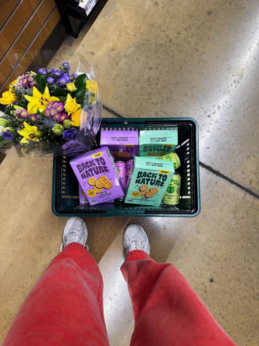 A Whole Foods shopping basket full of mini seasoned crackers and color coordinated flower bouquet