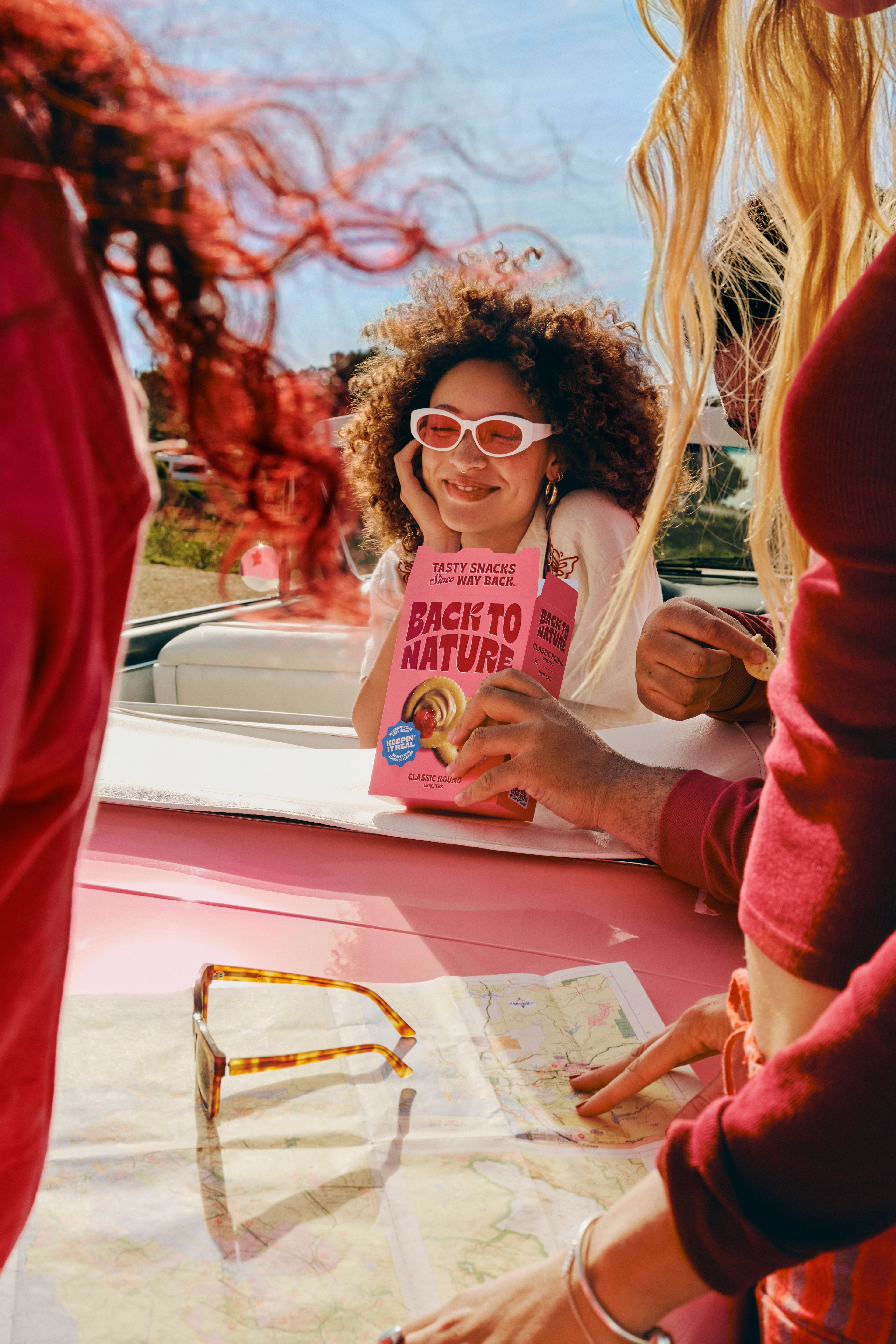 Friends leaning over a pink convertible eating crackers