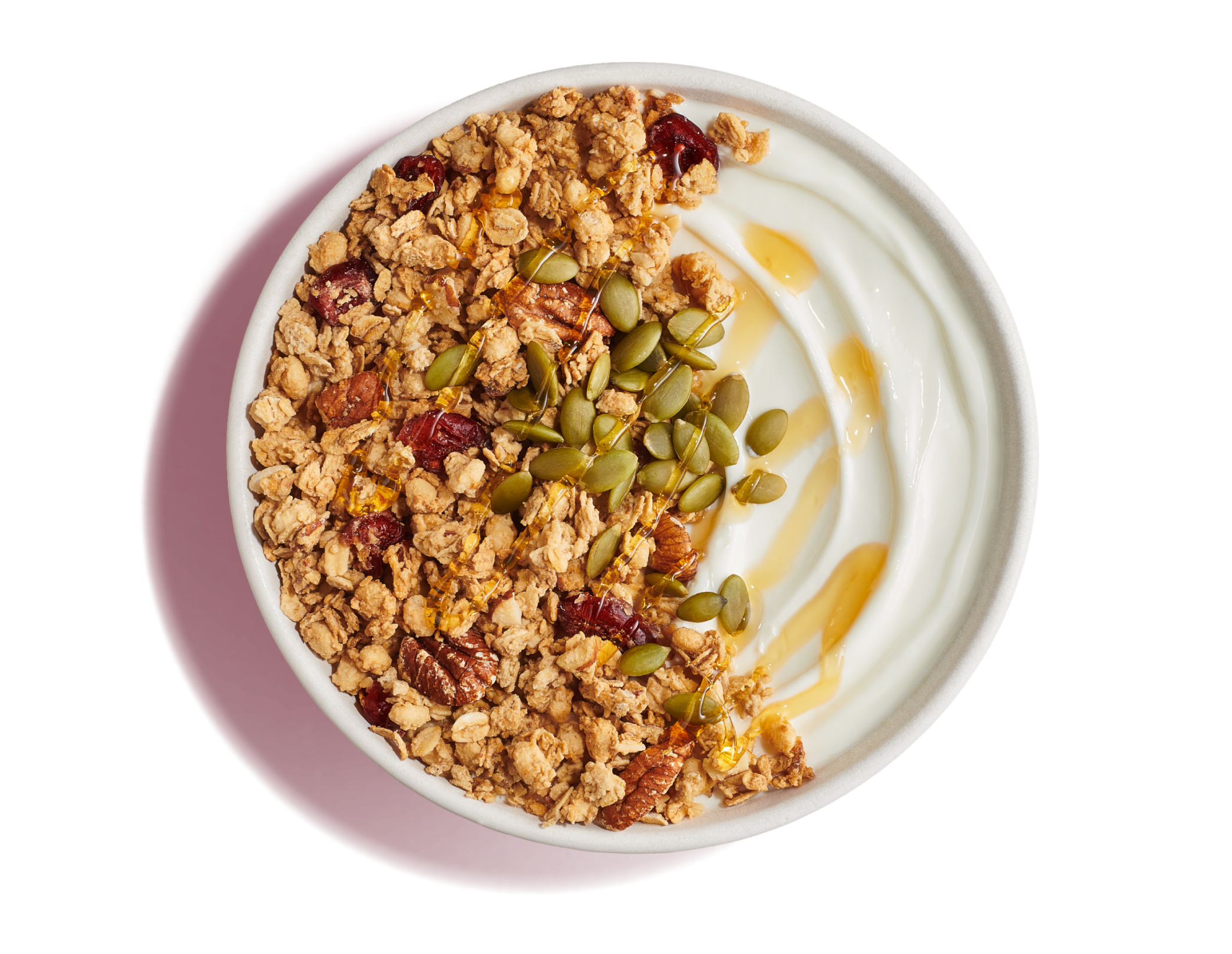White bowl of plain yogurt with golden, crunchy granola, pecans, and dried cranberries topped with seeds and honey on a deep pink background.