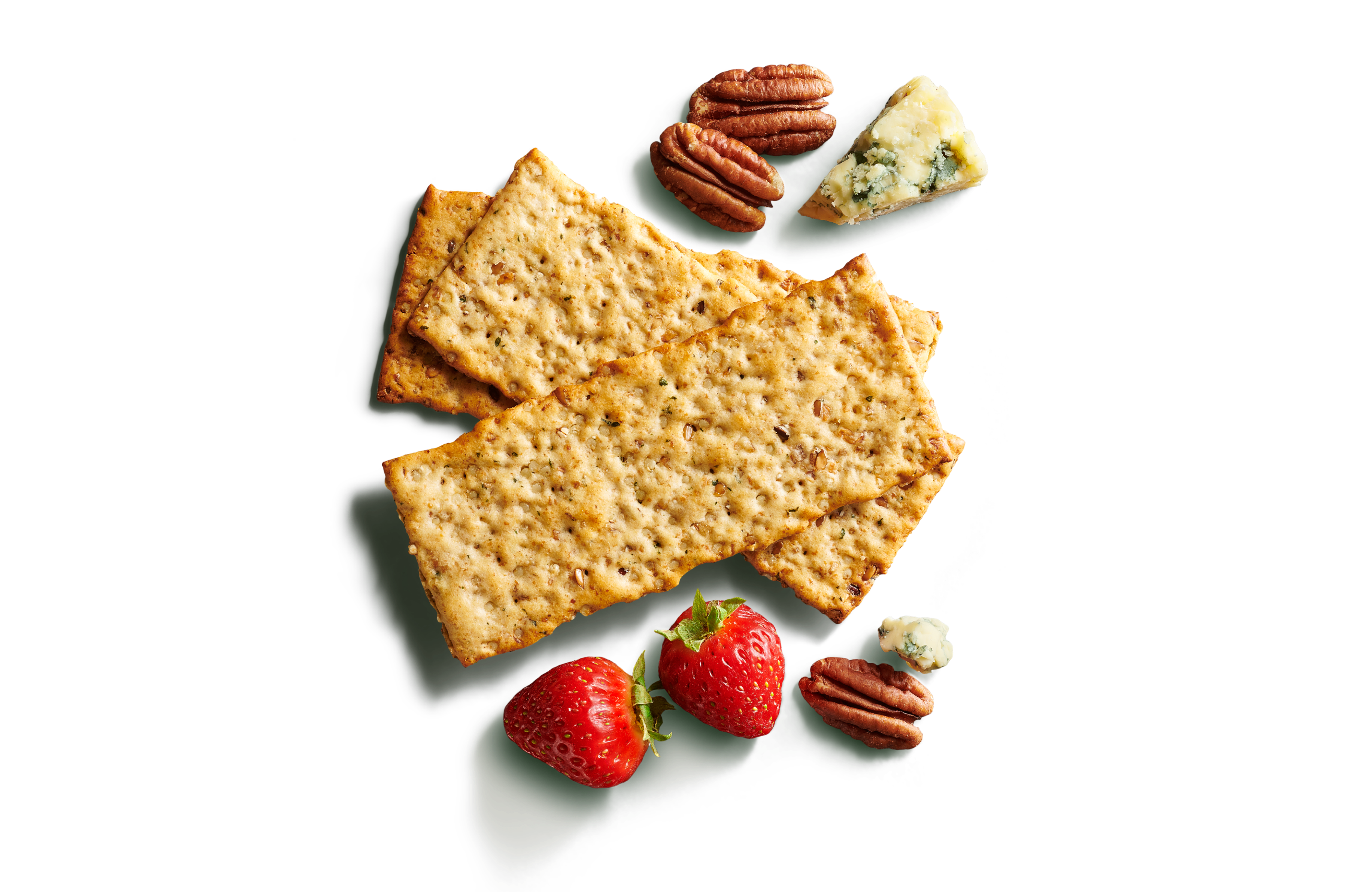 Close-up of three layered long, multigrain crackers on a bright green background with pecans, blue cheese, and strawberries.