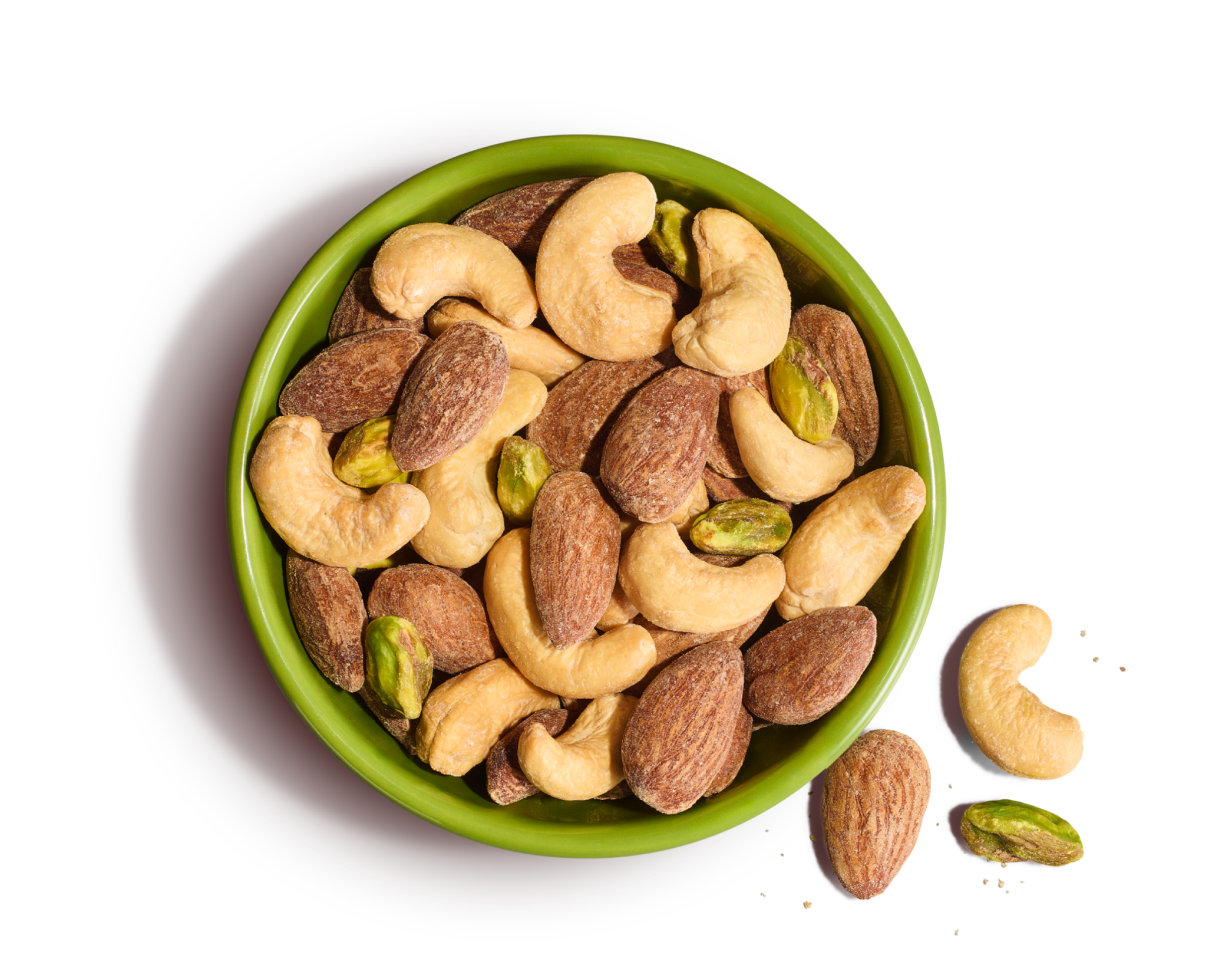 Green bowl of whole cashews, pistachios, and almonds on an orange background.
