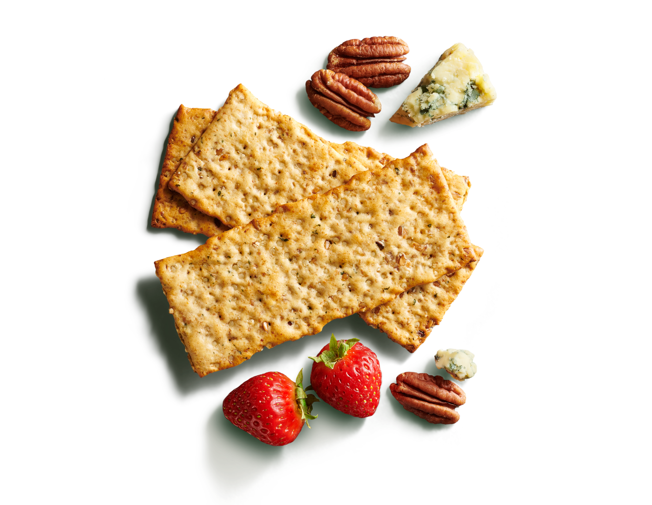 Close-up of three layered long, multigrain crackers on a bright green background with pecans, blue cheese, and strawberries.