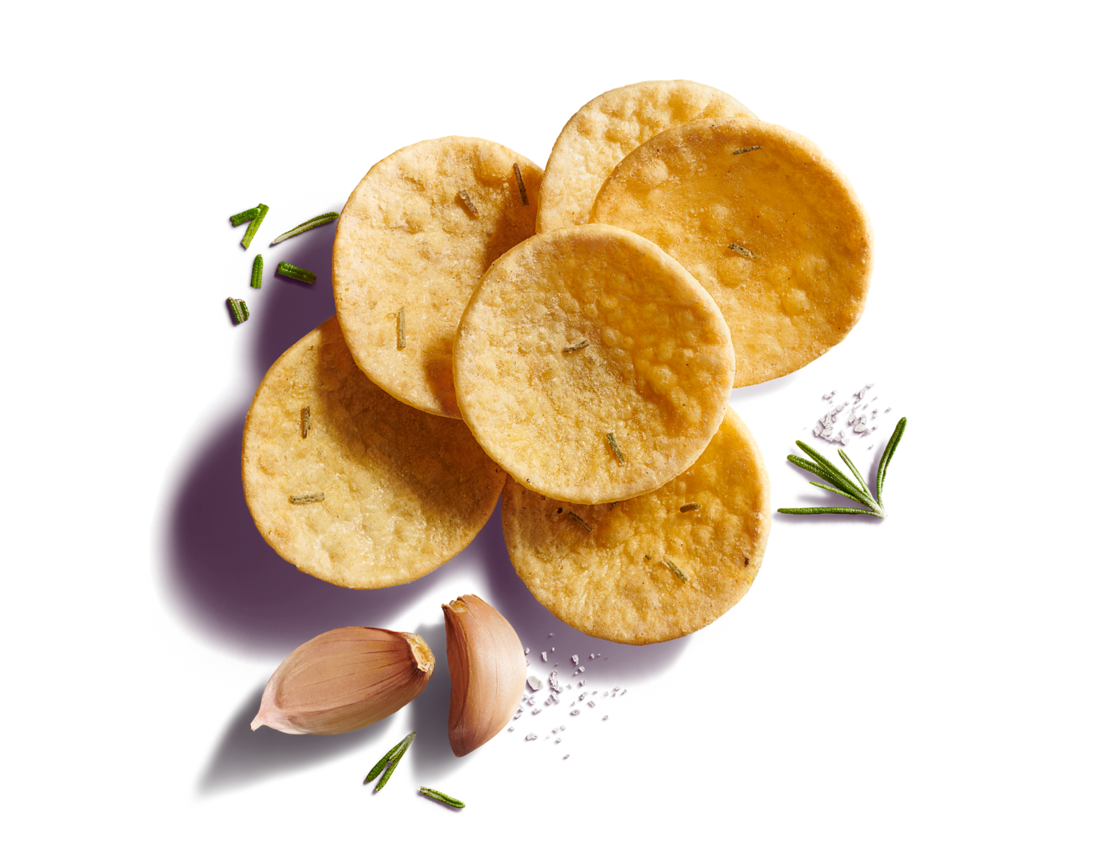 Close-up of six scattered round, curved scoop crackers on a bright purple background with garlic cloves, rosemary, and sea salt flakes.