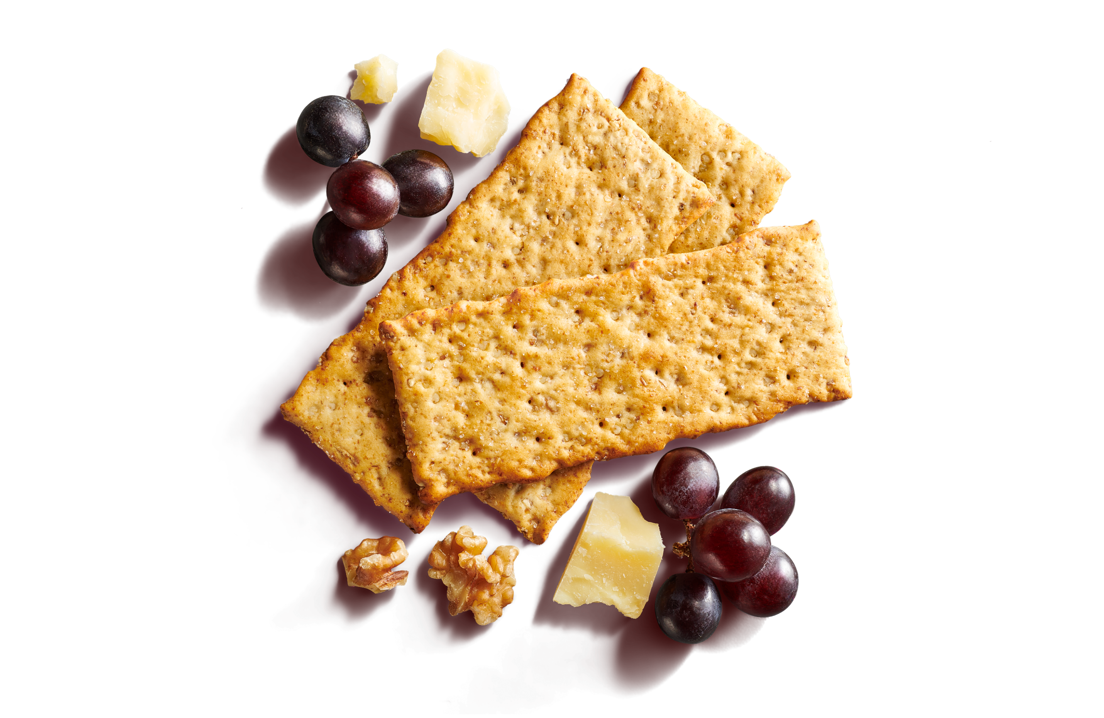 Close-up of three layered long crackers on a pale pink background with grapes, walnuts, and cheese. 