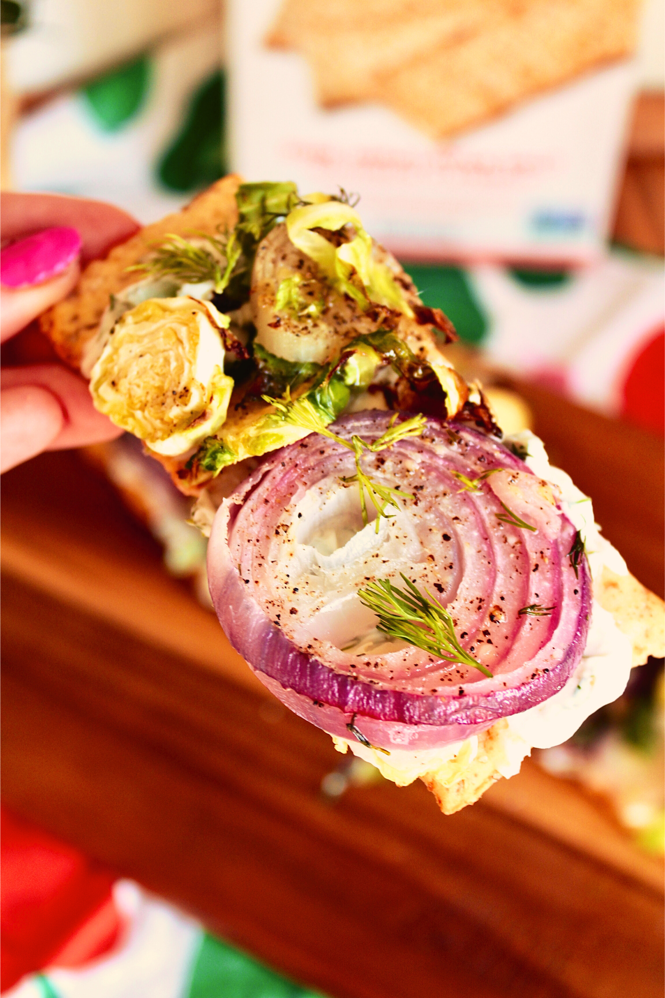 A hand holding an onion & brussels sprout flatbread cracker