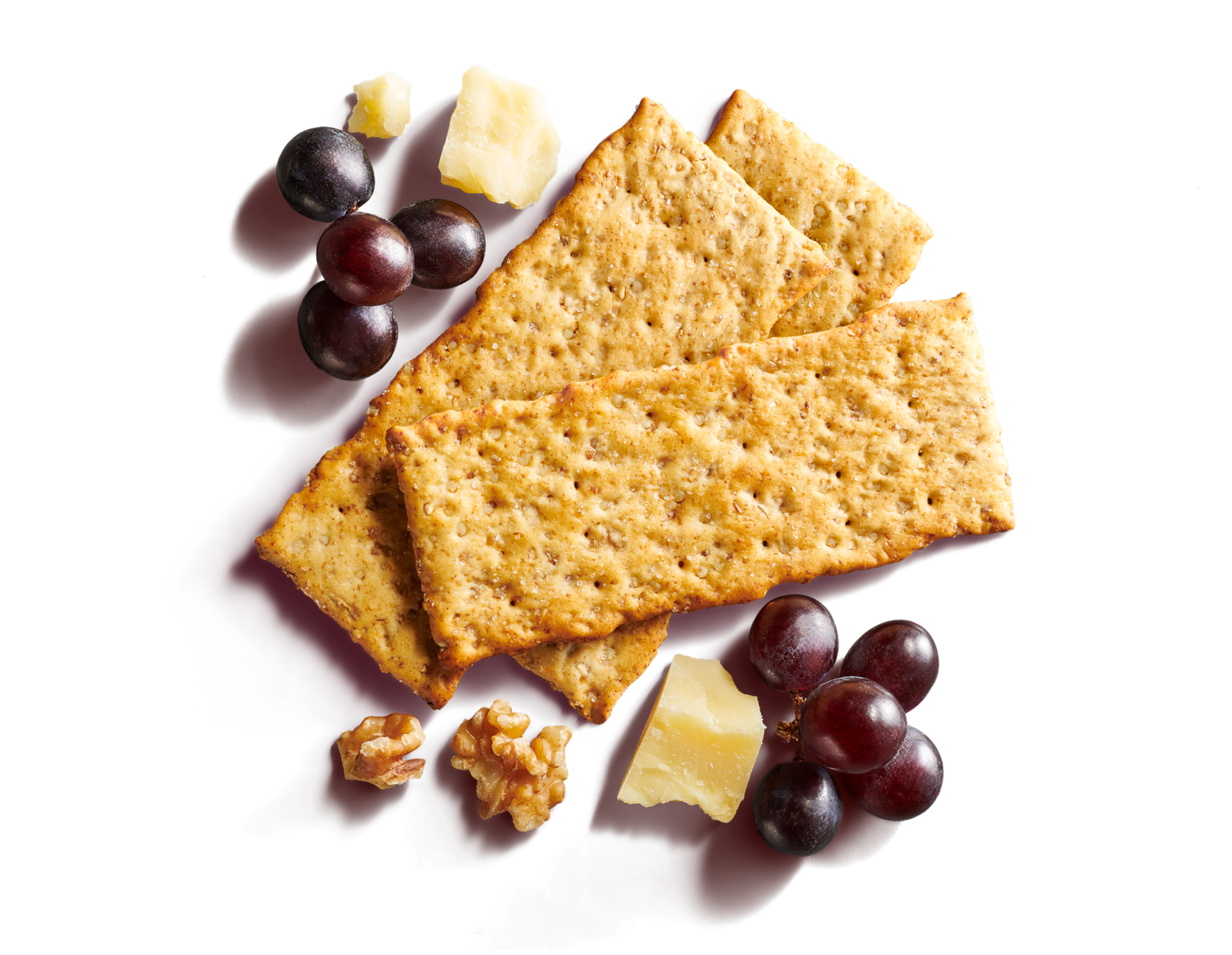 Close-up of three layered long crackers on a pale pink background with grapes, walnuts, and cheese. 