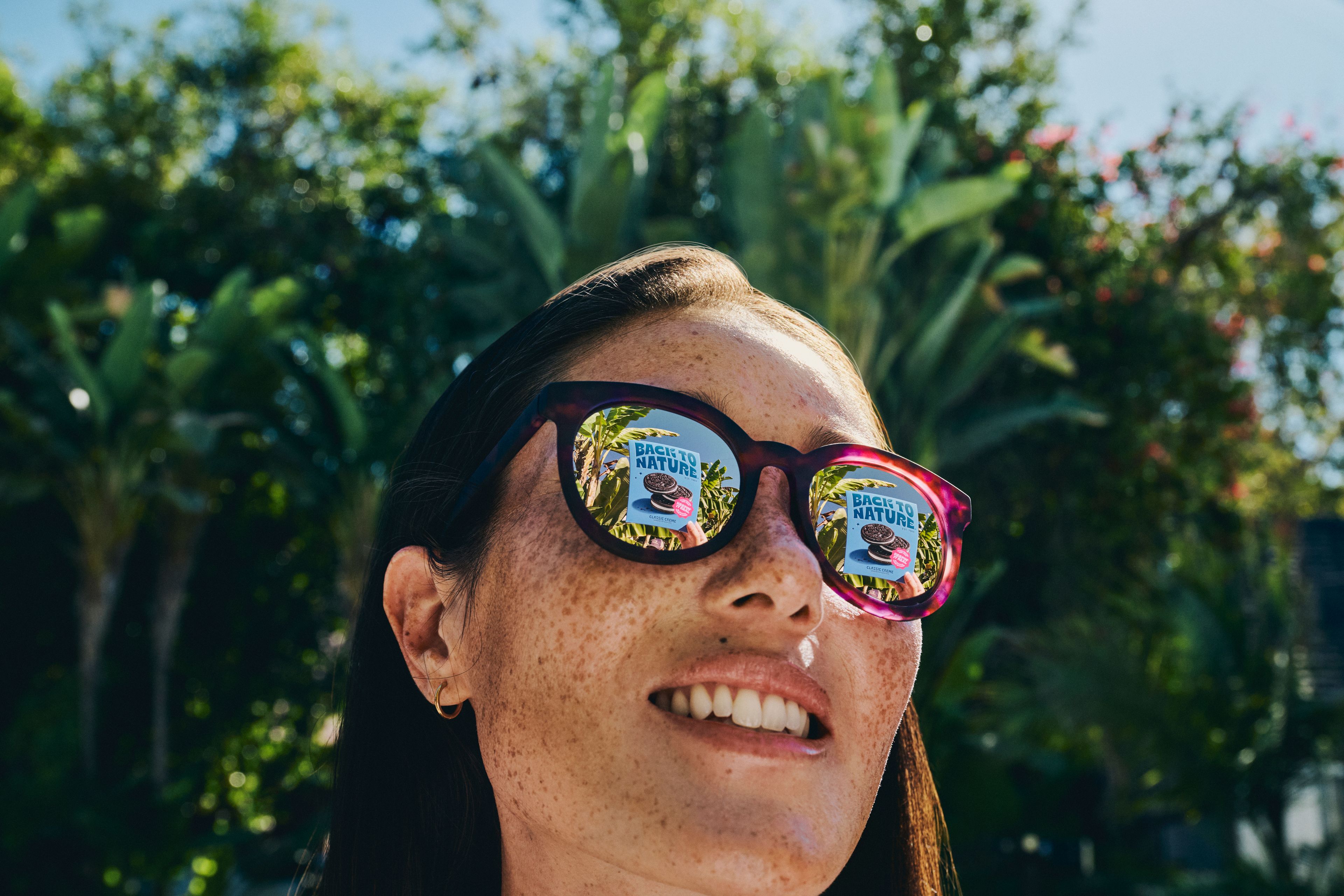 A woman wearing sunglasses and smiling, cookies are reflected in the lenses