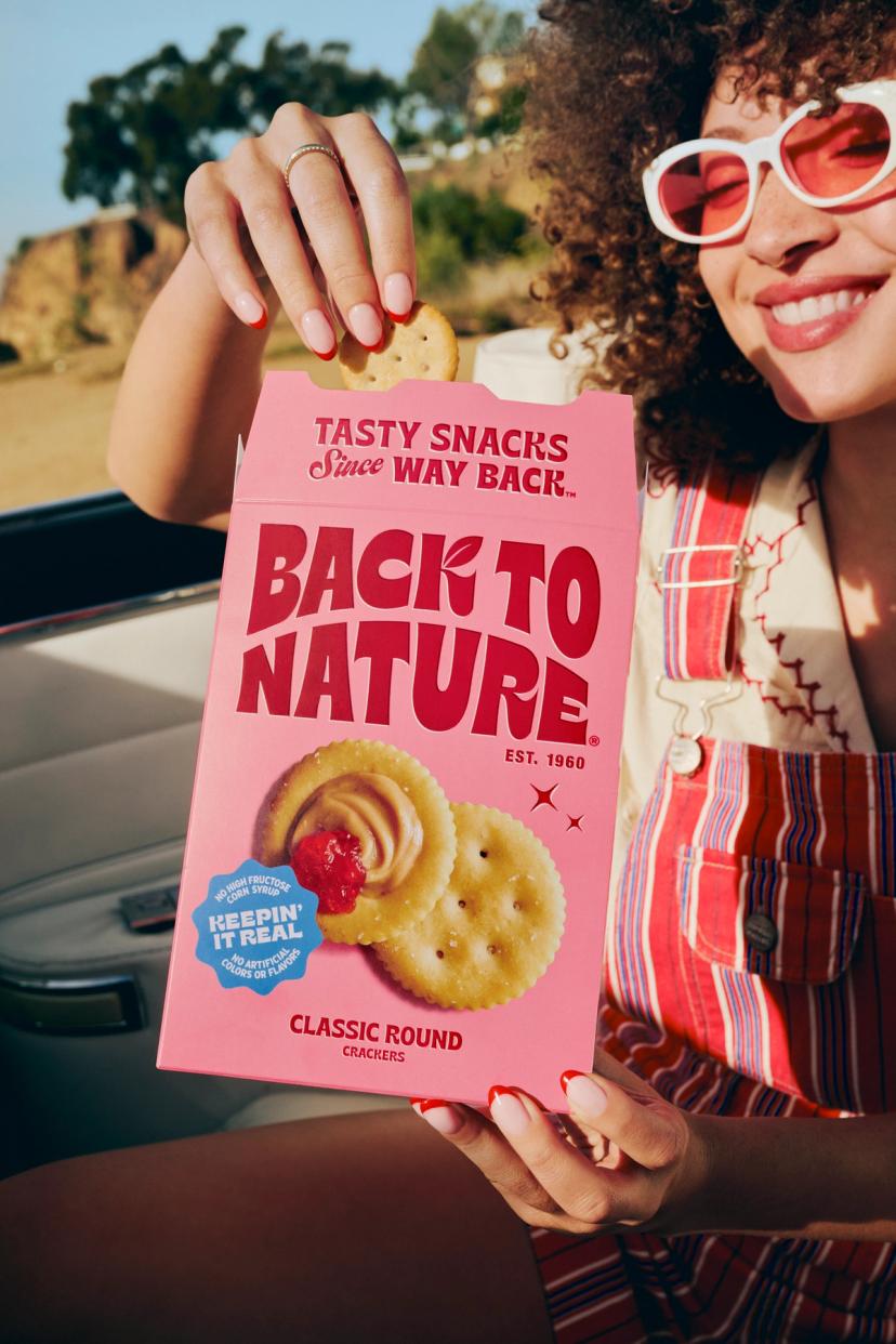 A woman with curly hair eating classic round crackers, smiling