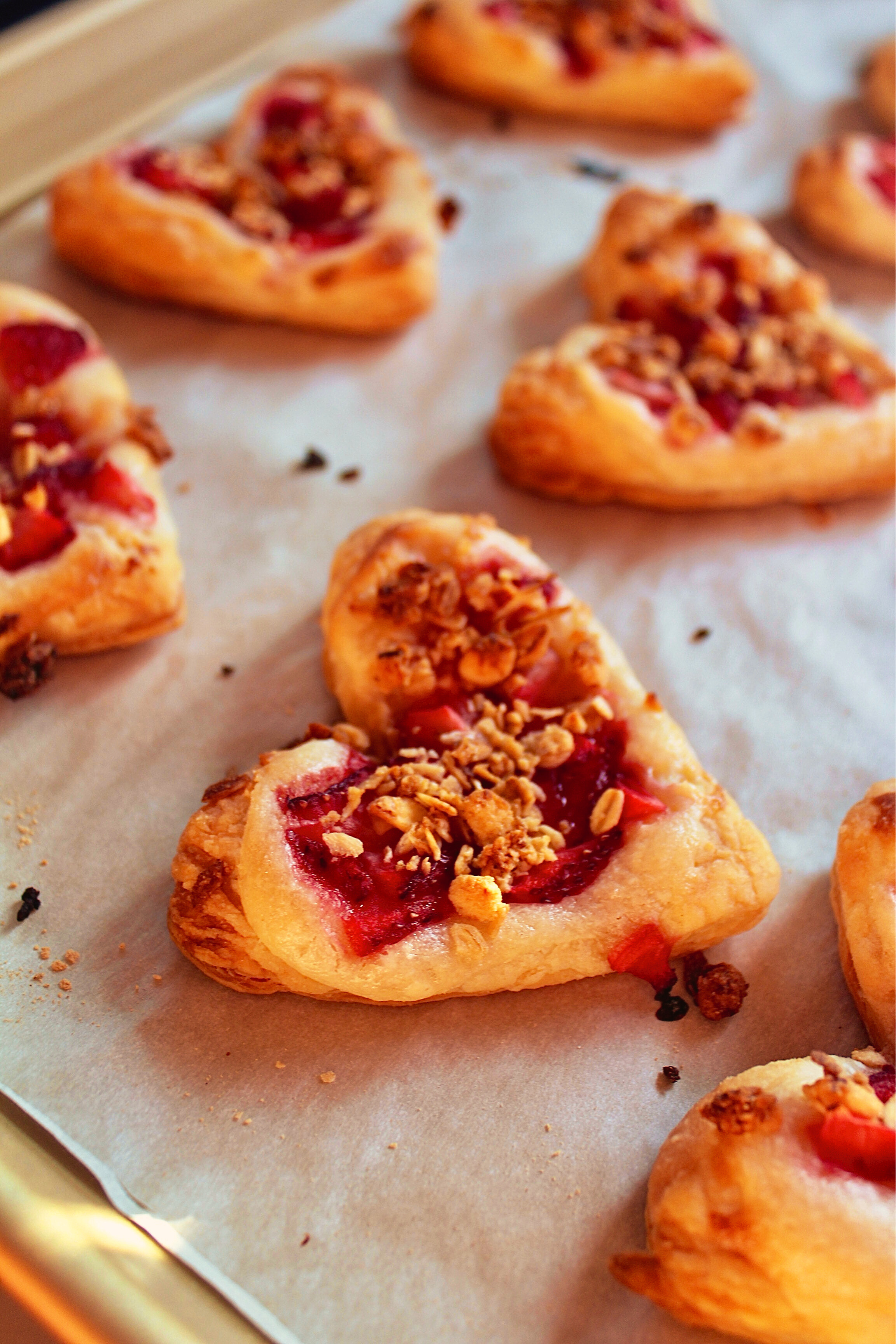 Puff pastry hearts topped with jam and granola on a baking sheet