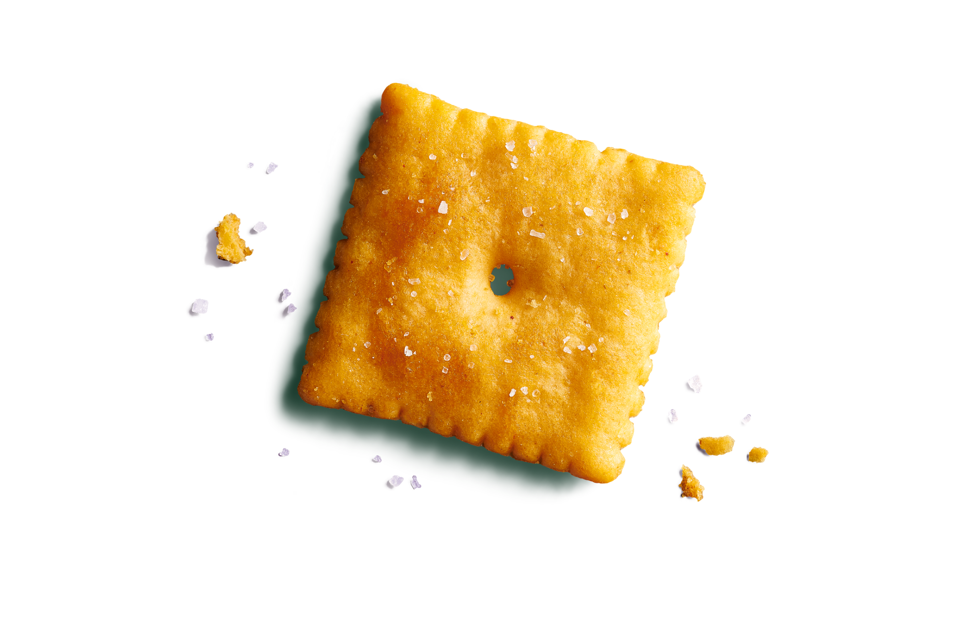 Close-up of one large cheesy, orange square cracker on a vibrant seafoam green background with salt flakes and cheese crumbs.
