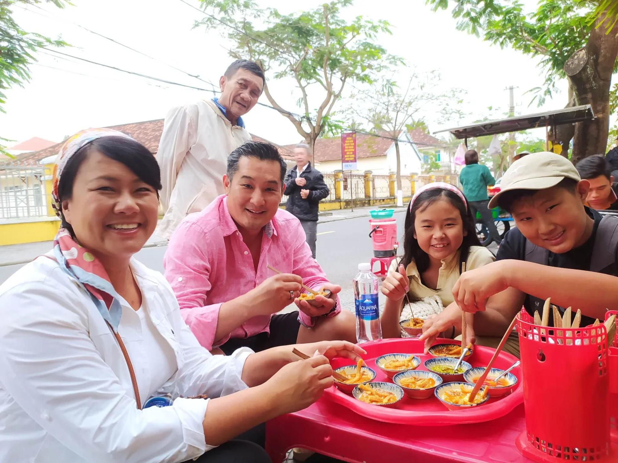 Travellers tasting freshly made Hoi An street snacks with a local vendor at her red table on a Fingo private food tour.