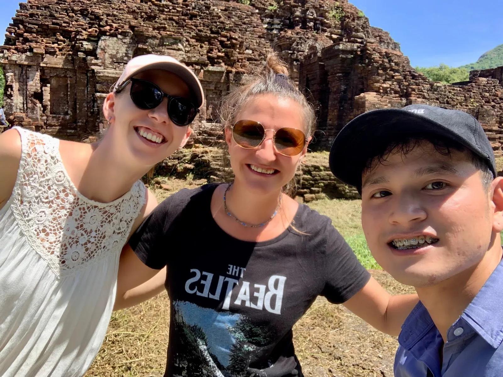 Fin from Fingo Private Tours smiling in a selfie with two guests in front of the Cham brick temples at My Son Sanctuary.