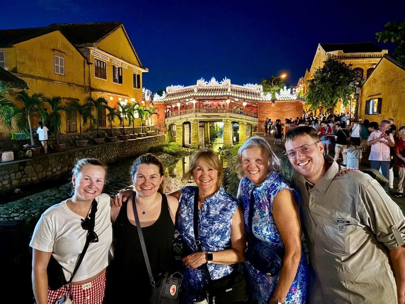 Smiling private group in front of the illuminated Japanese Covered Bridge in Hoi An Ancient Town at night on a Fingo private walking tour.