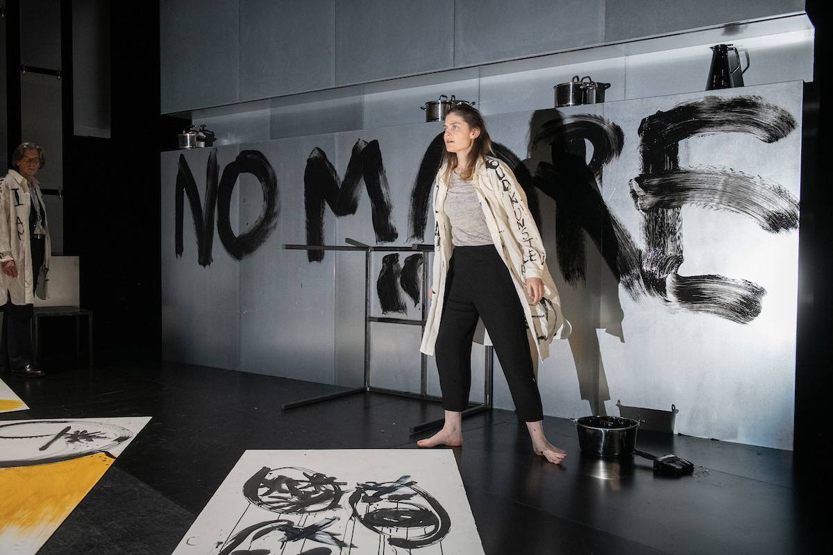 a performer with "no more" painted on the wall behind her
