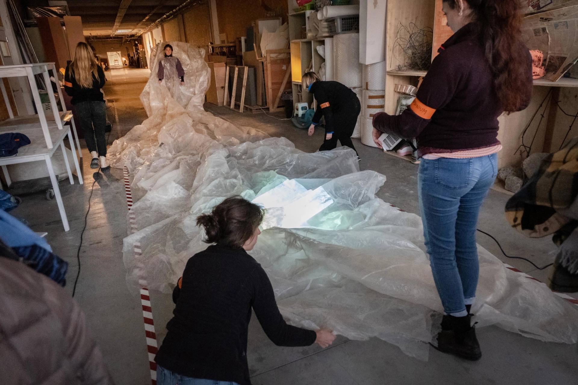 a woman and other women helping her walk with a giant plastic dress