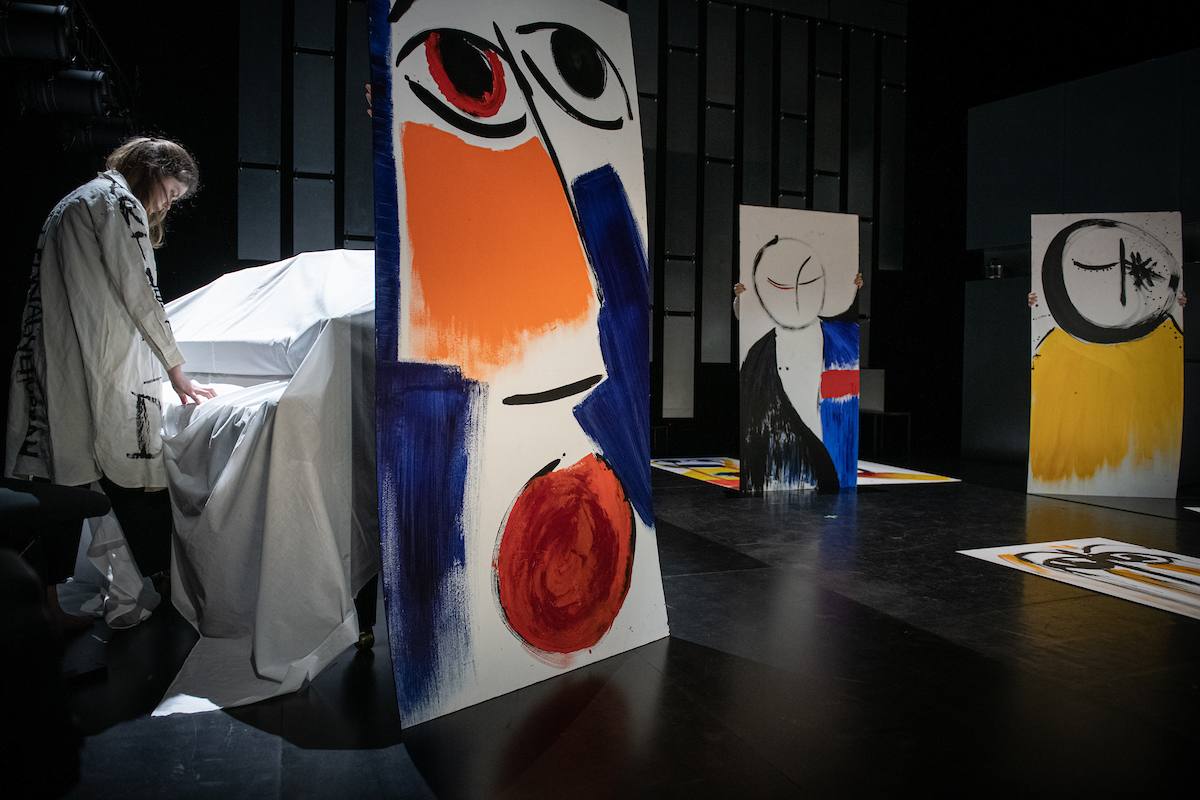 a woman at the piano singing to her paintings on stage