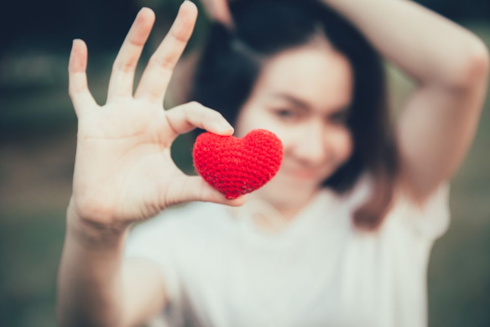 Woman holding red heart in focus symbolizing first Valentine’s Day after divorce and emotional healing