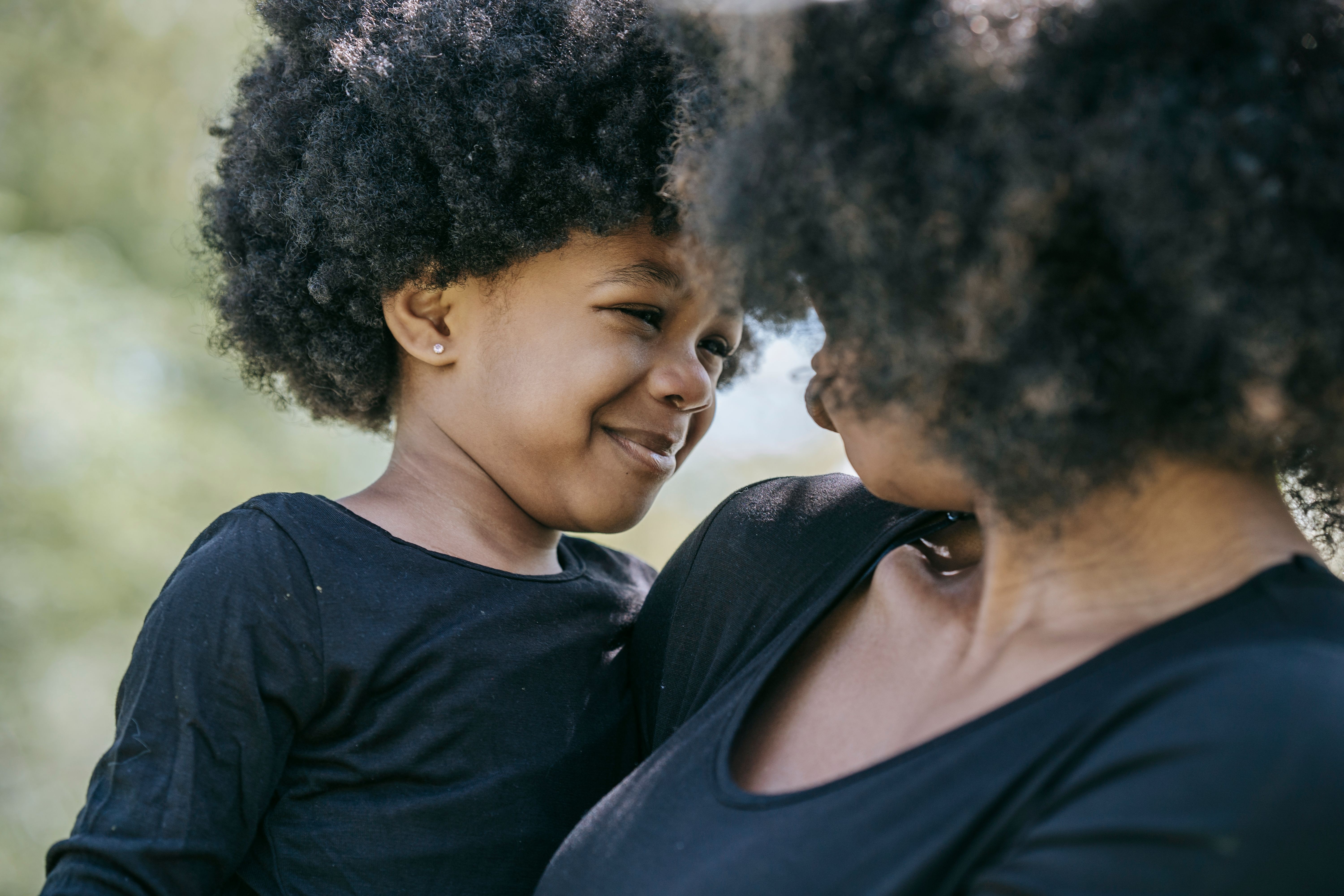 Image A young girl smiles warmly at her mother while being held outdoors, illustrating the parent-child bond at the heart of post-divorce parenting decisions in Illinois.