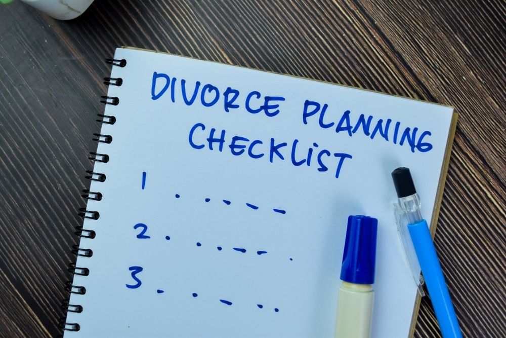 A notebook titled "Divorce Planning Checklist" on a wooden desk with a blue marker.