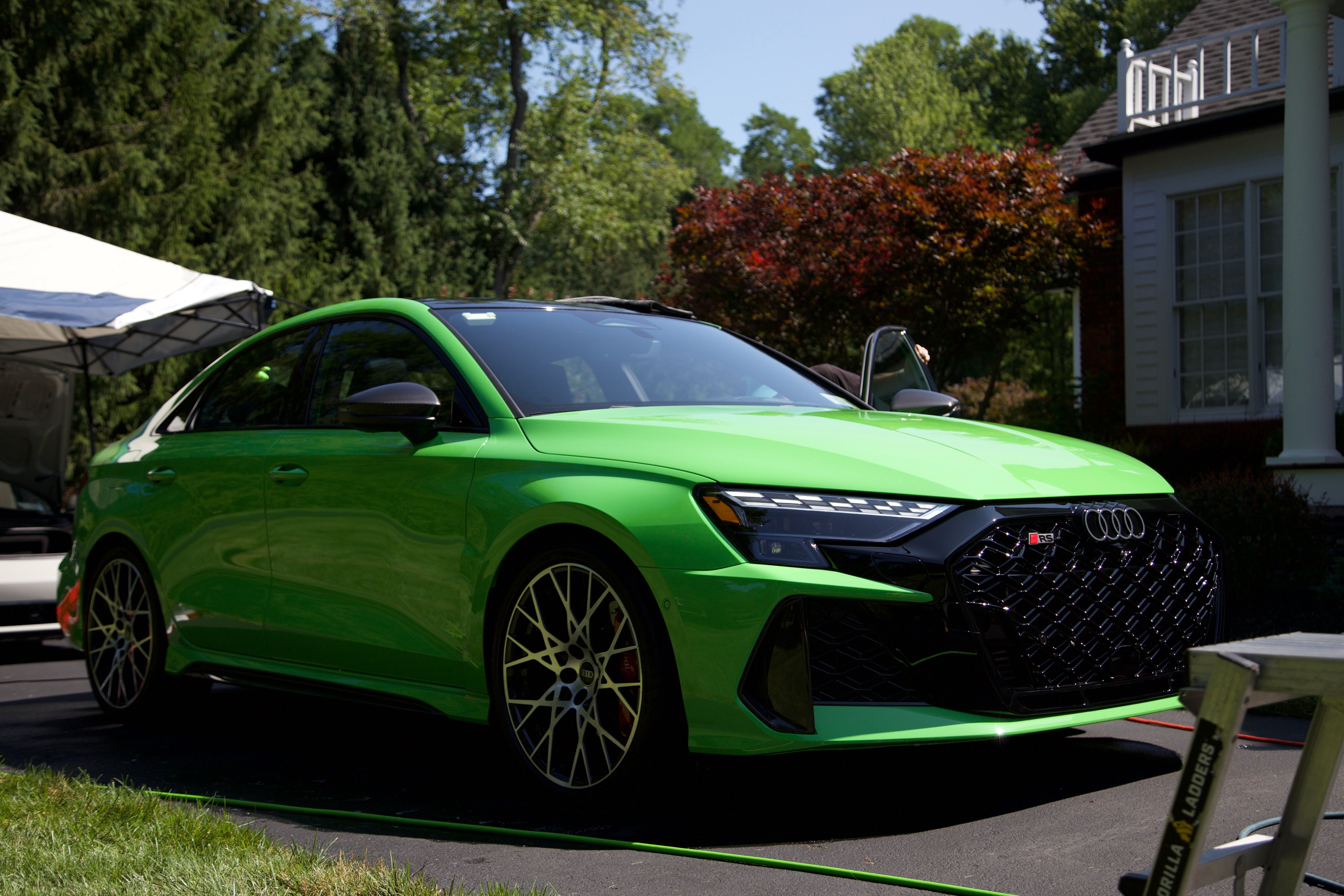 A bright green Audi RS3. In the background is another vehicle under a canopy and in the foreground is a work platform slightly out of view.