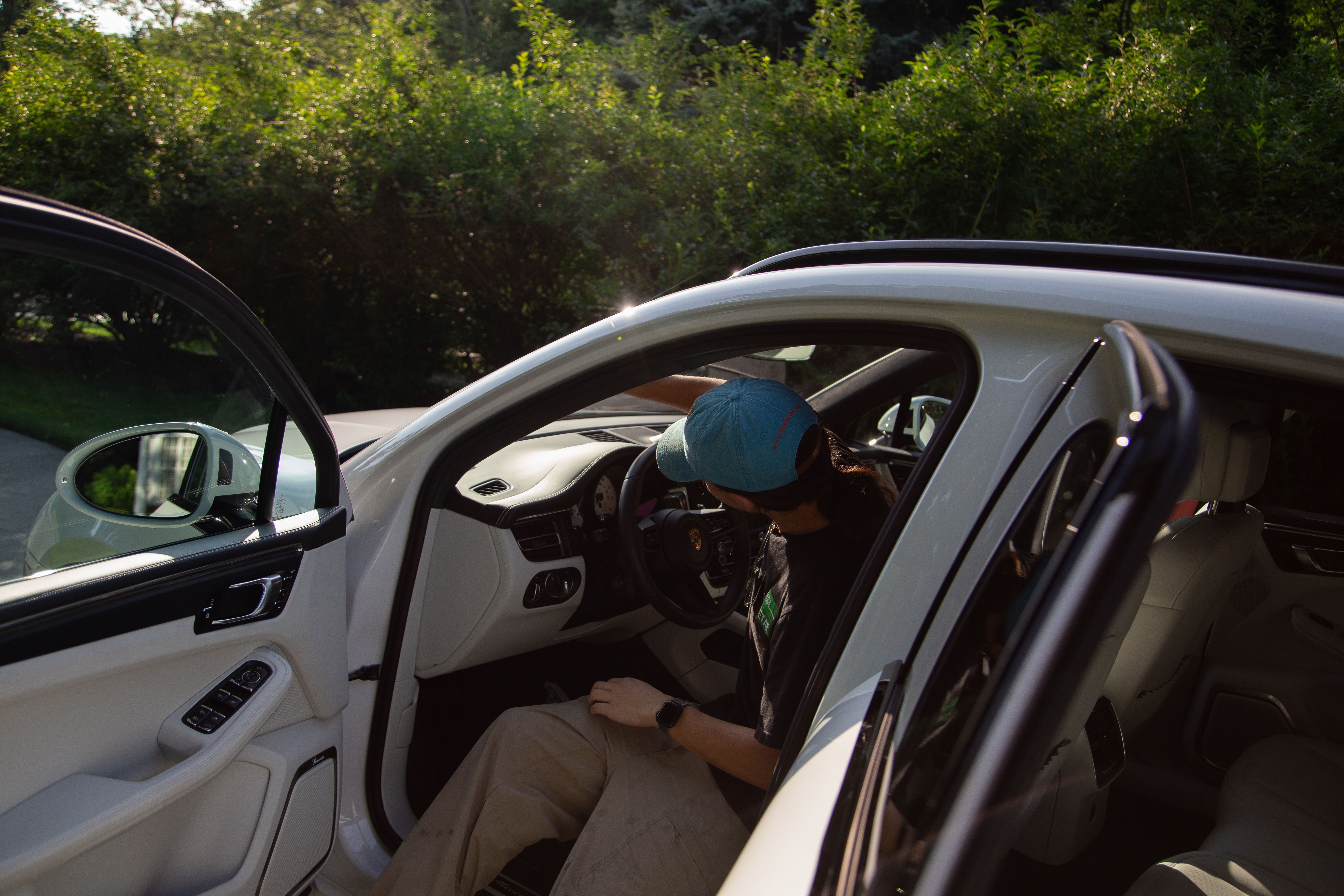 A M&L Detailing Technician cleaning the interior windshield on a white Porsche Macan.