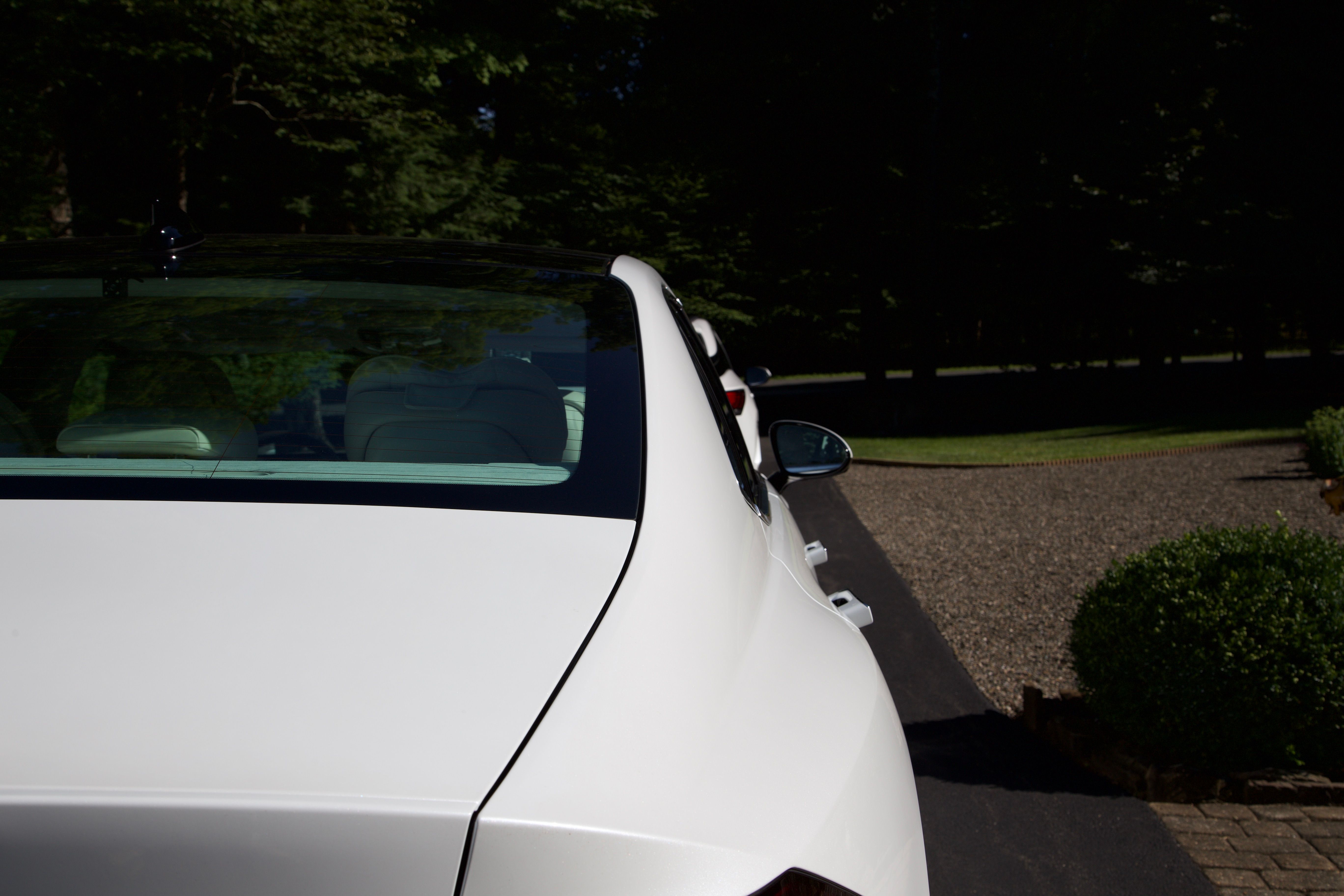 A rear side profile image of a white Genesis G90. The paint is gleaming, and there is a second white car directly behind it.