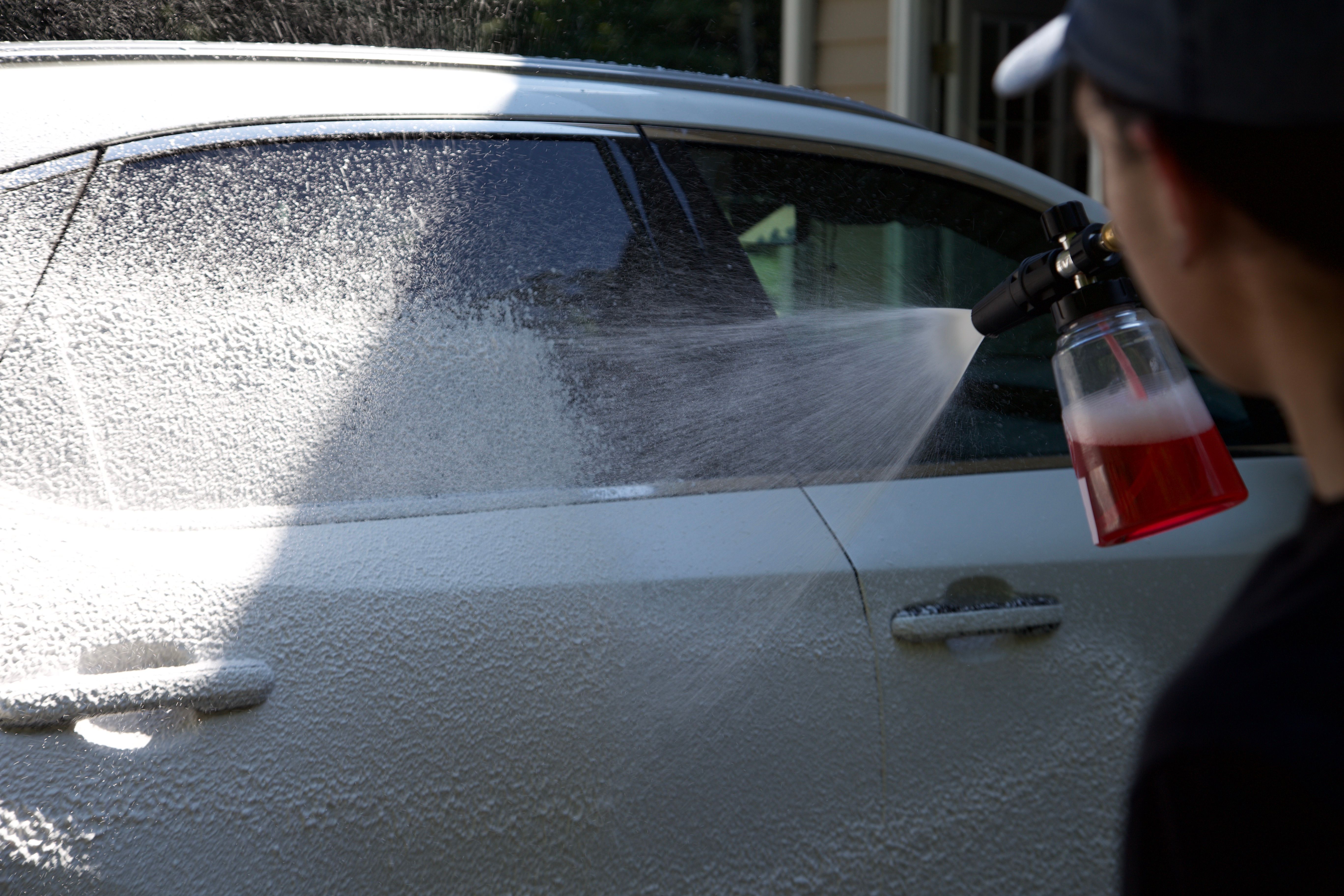 A M&L Detailing Technician spraying soap onto a white car.