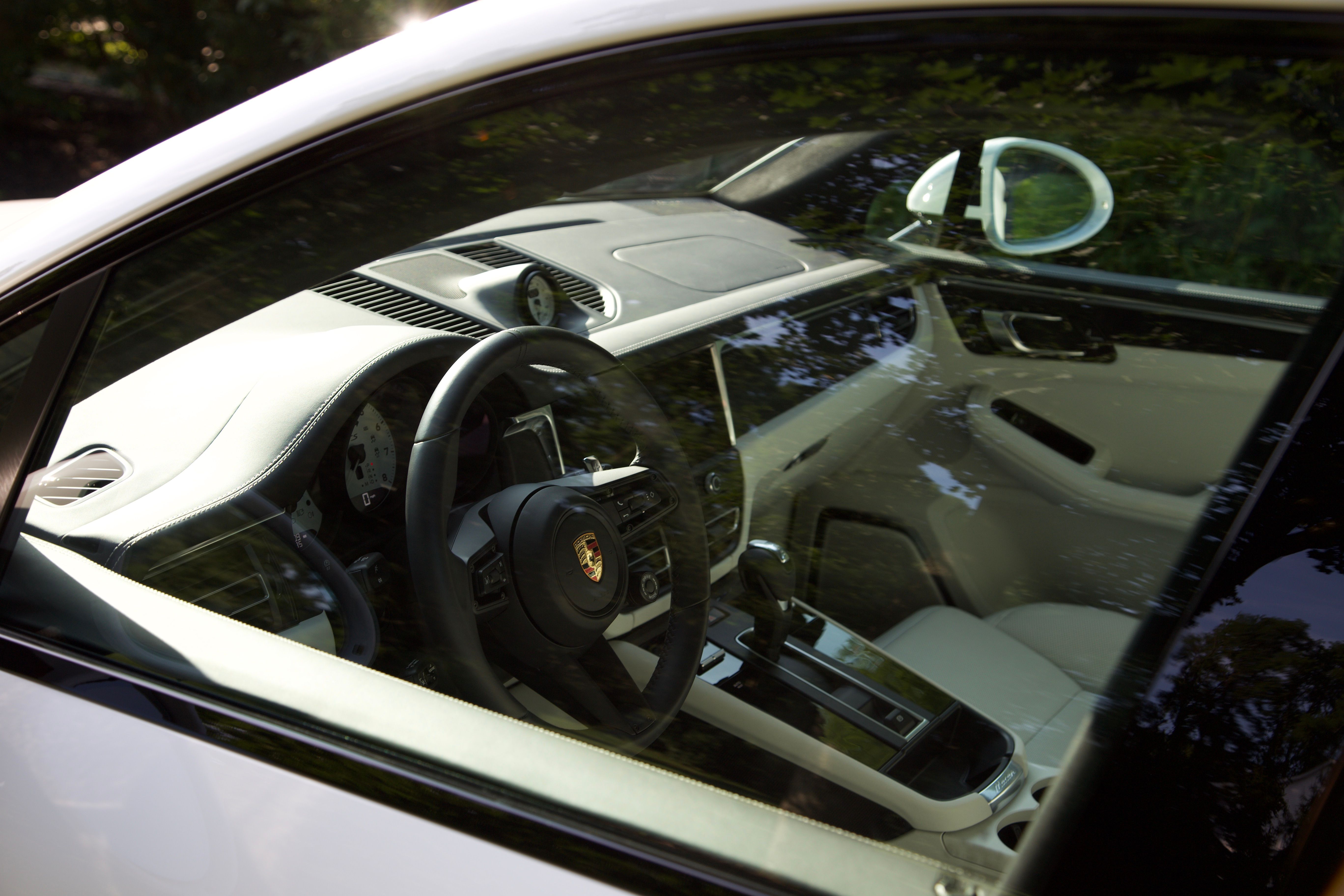 The interior of a white Porsche Macan. The image is taken from the drivers side through the window glass.