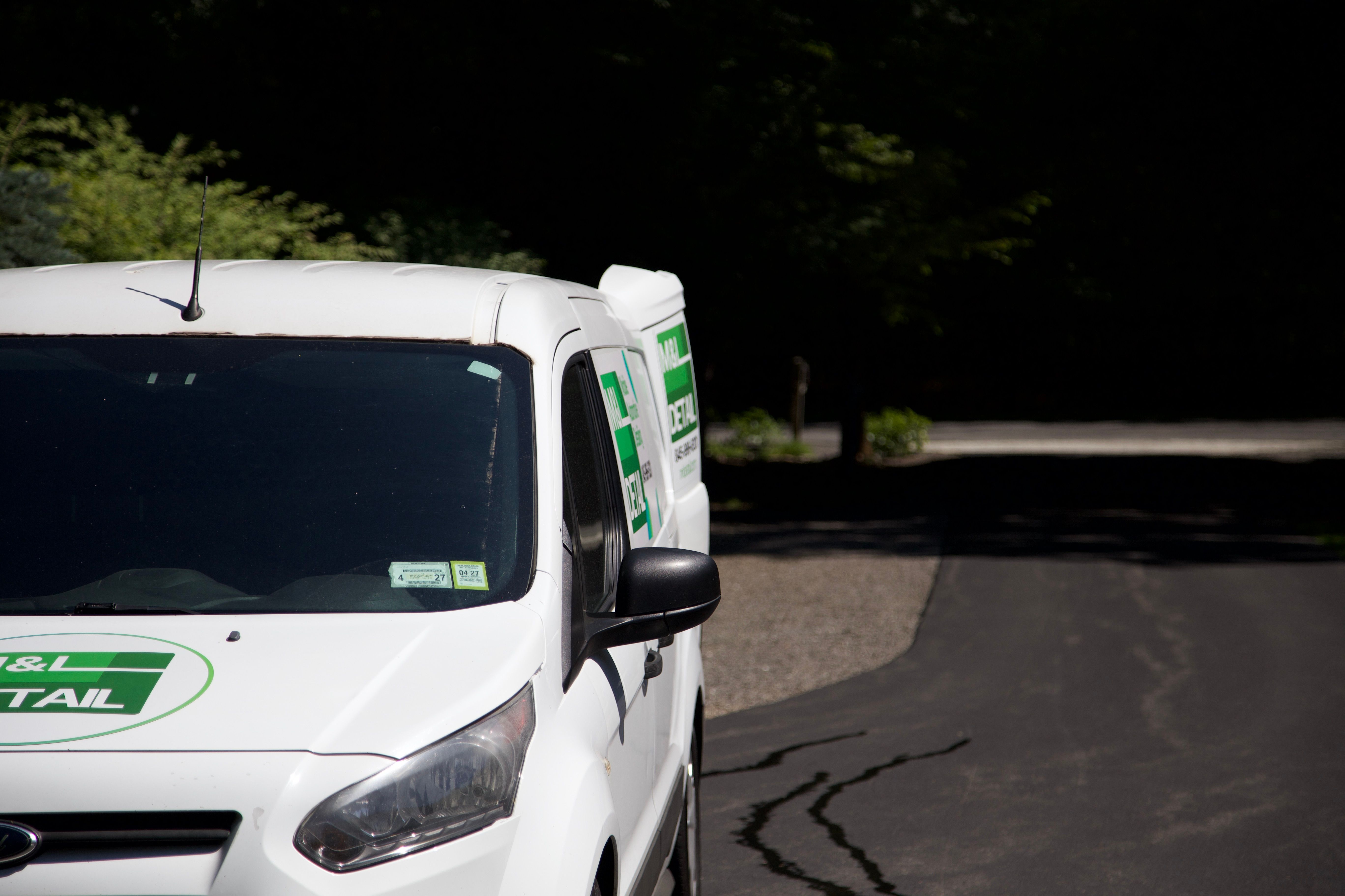 A white Ford Transit Connect displaying the M&L Detail logo on the hood, driver side door, and driver side rear door.