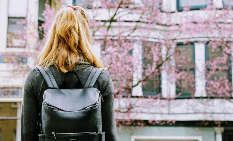 Kuvassa nainen seisoo selin kameraan, taustalla asuinrakennus ja kukkiva kirsikkapuu