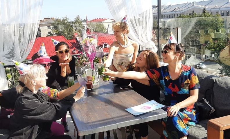 Kuvassa kuusi naista istumassa kahvilan pöydän ääressä