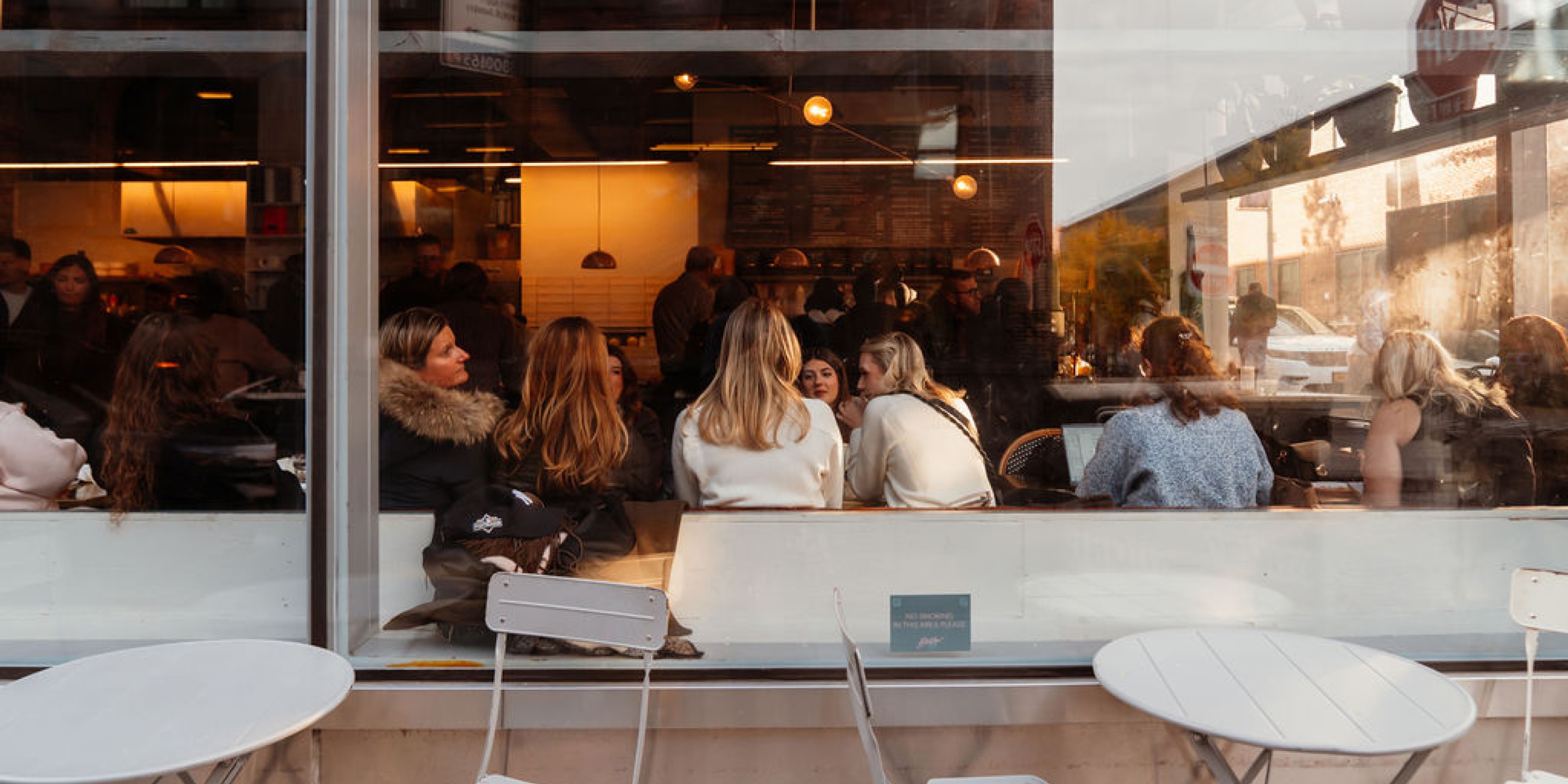 Crowded café interior viewed through a window, with groups of people sitting and talking inside.