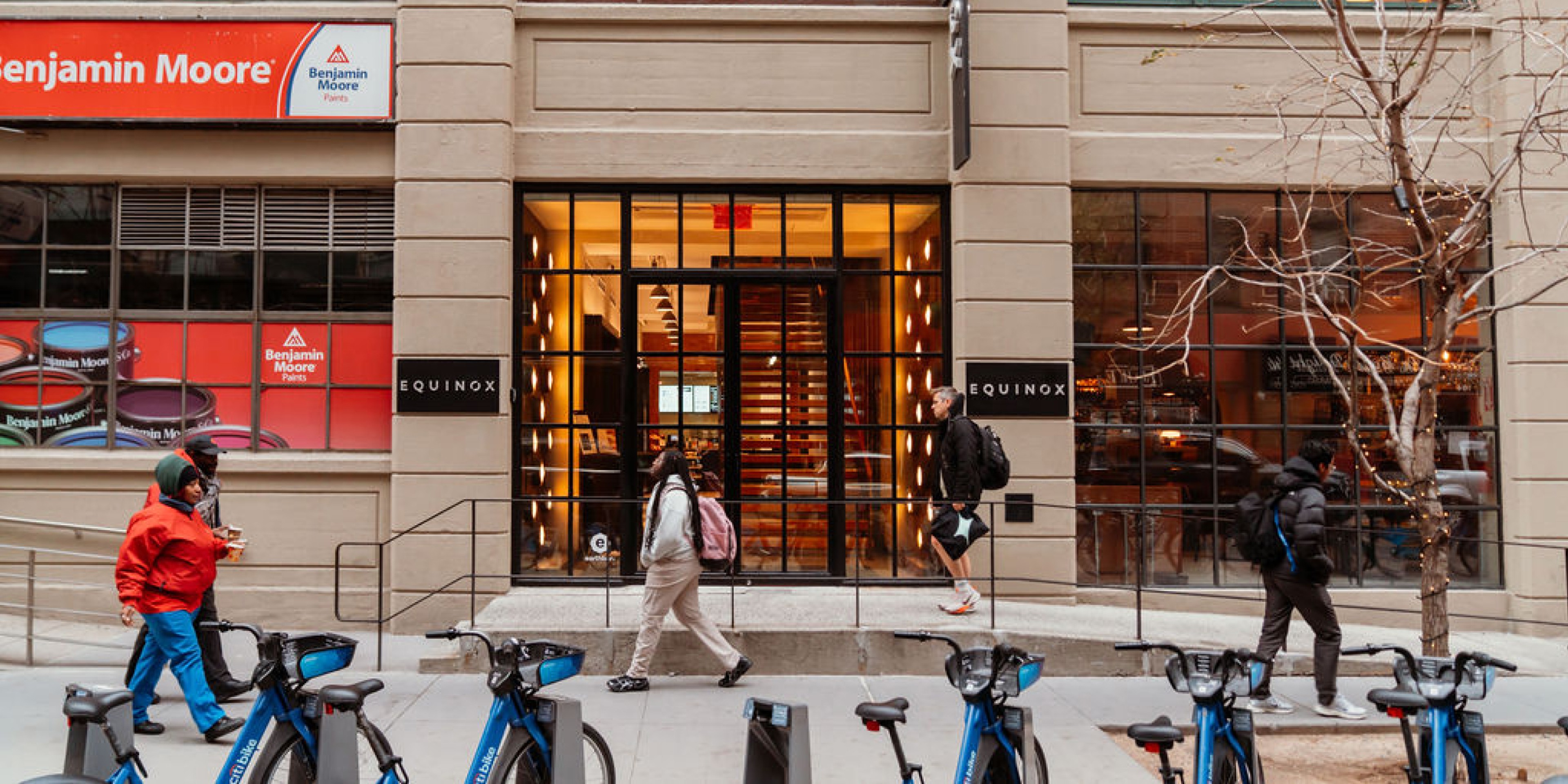 Street view of an Equinox gym entrance with people walking by and Citi Bikes parked along the sidewalk outside.