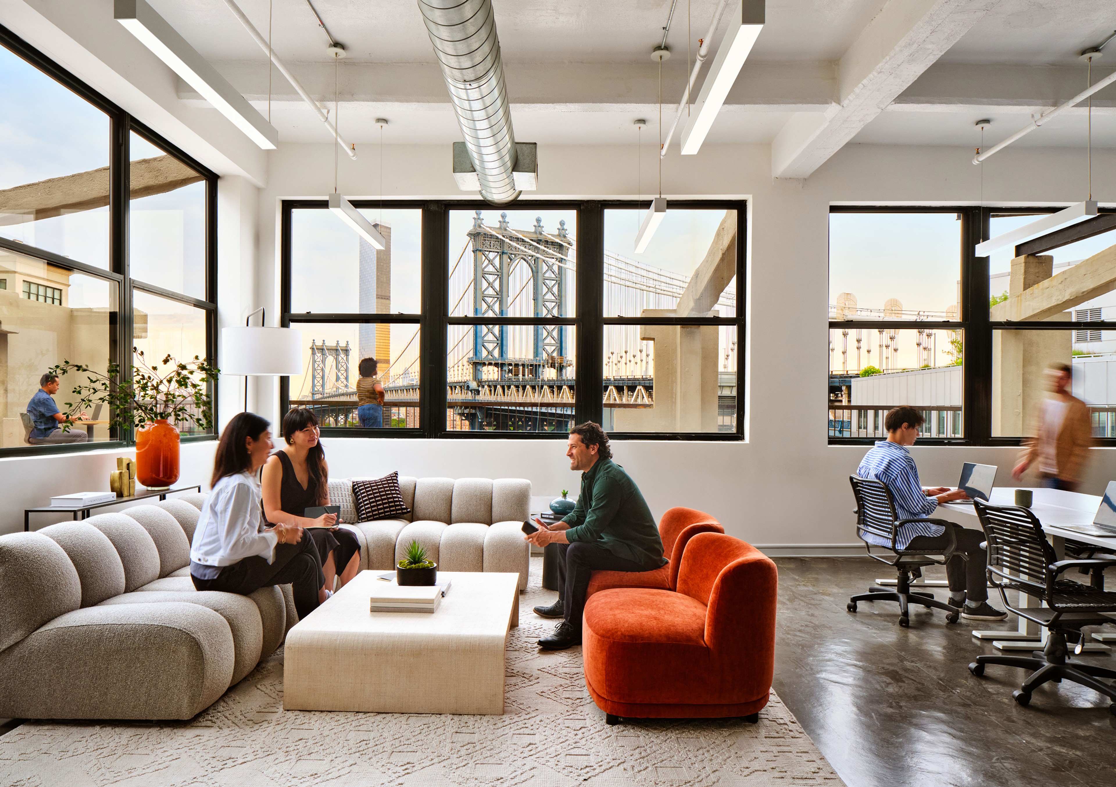People meeting on couches in front of window with view of the Manhattan Bridge