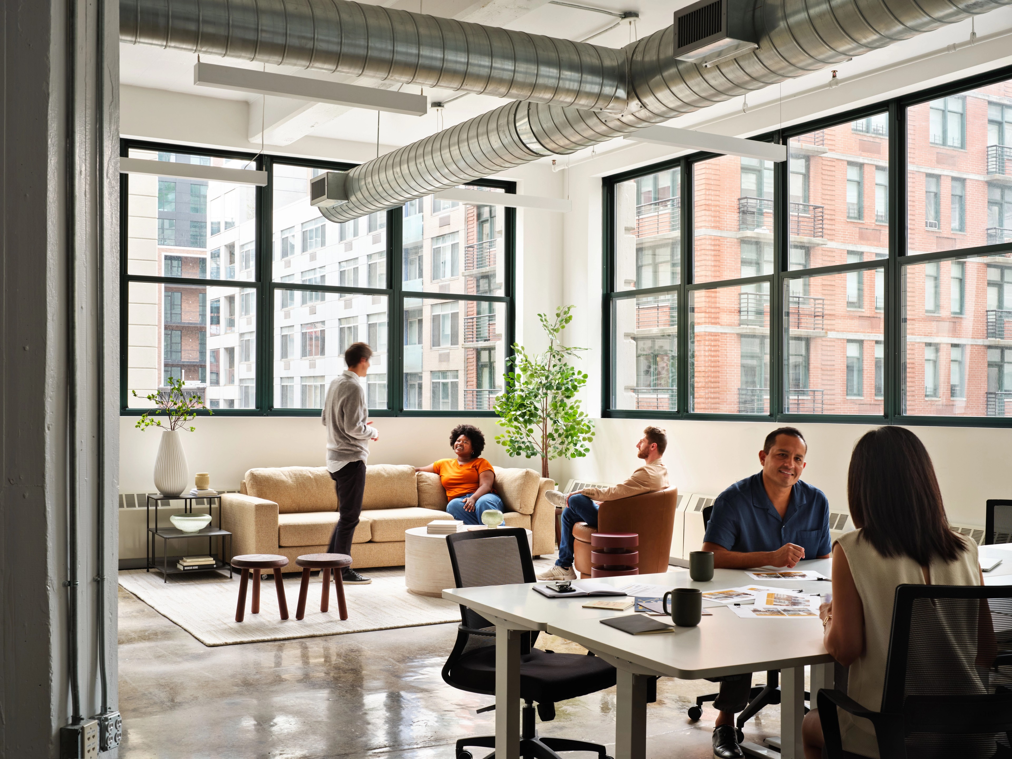 People working at a desk in a corner office with large windows