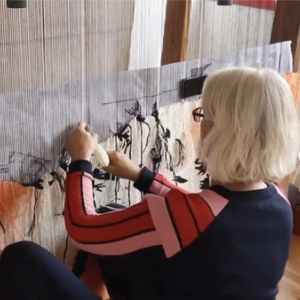 Videostillbilde av Kristin Sæterdal som arbeider med tekstil