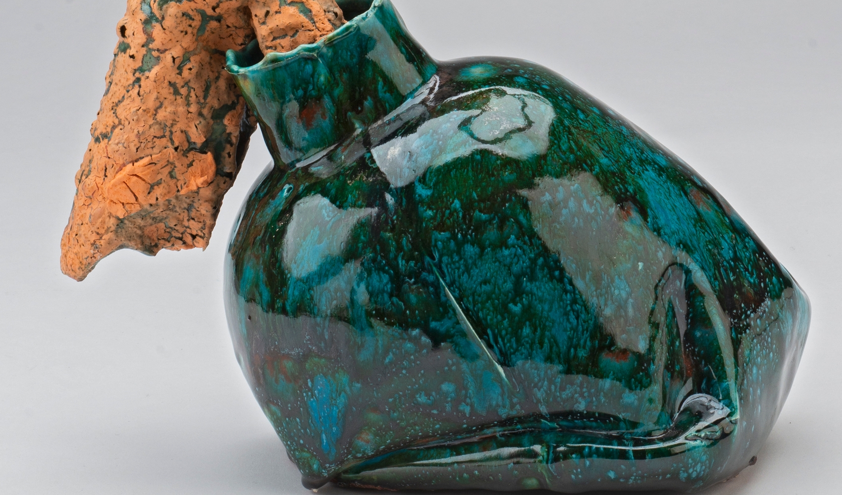 Vaselignende keramikkobjekt med grønn glasur, med en oransjefarget form som stikker ut av åpningen.