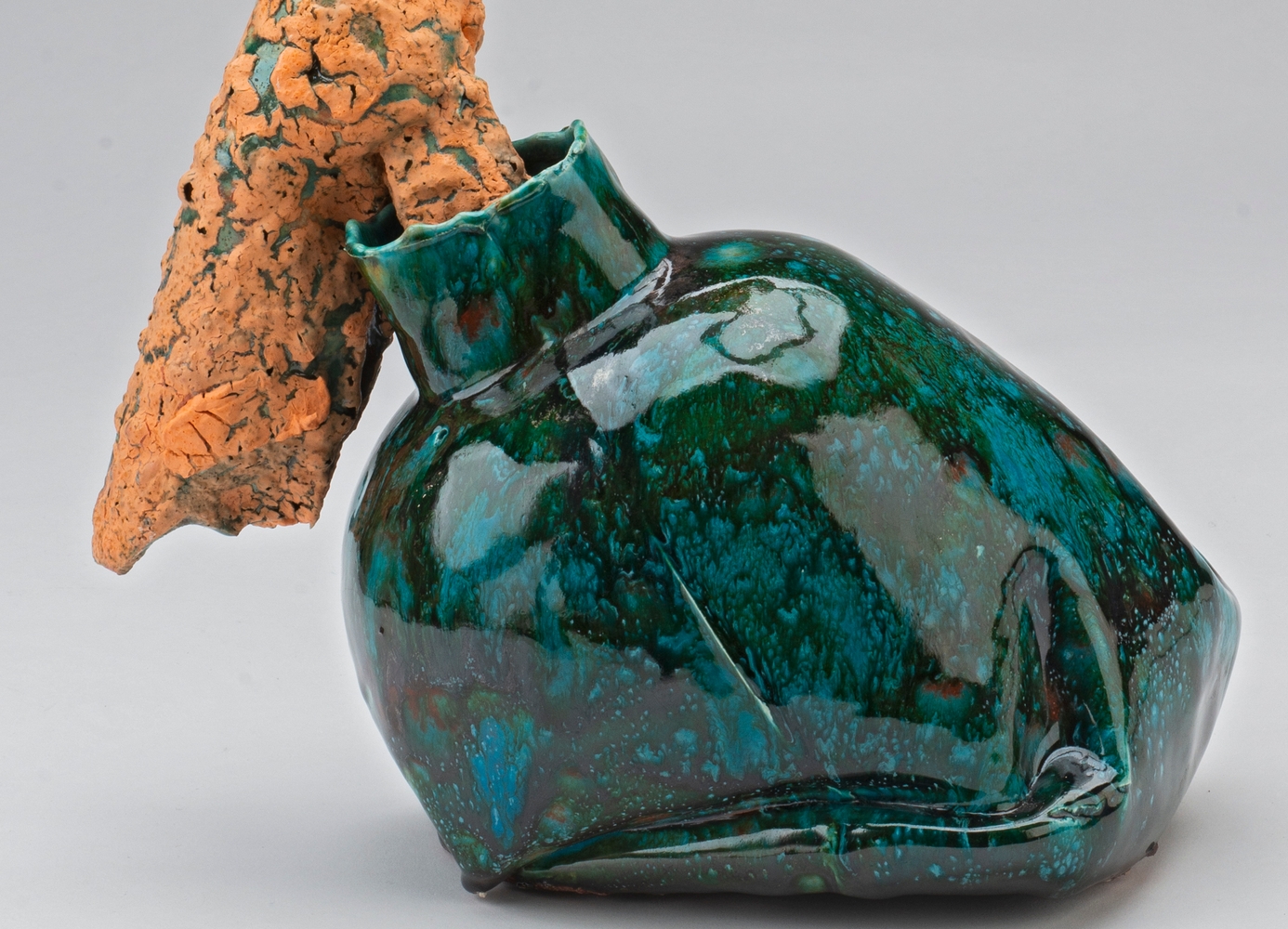 Vaselignende keramikkobjekt med grønn glasur, med en oransjefarget form som stikker ut av åpningen. 