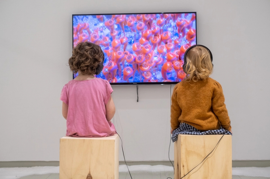 To barn ser på en skjerm med hodetelefoner. Skjermen er full av rosa maneter. 