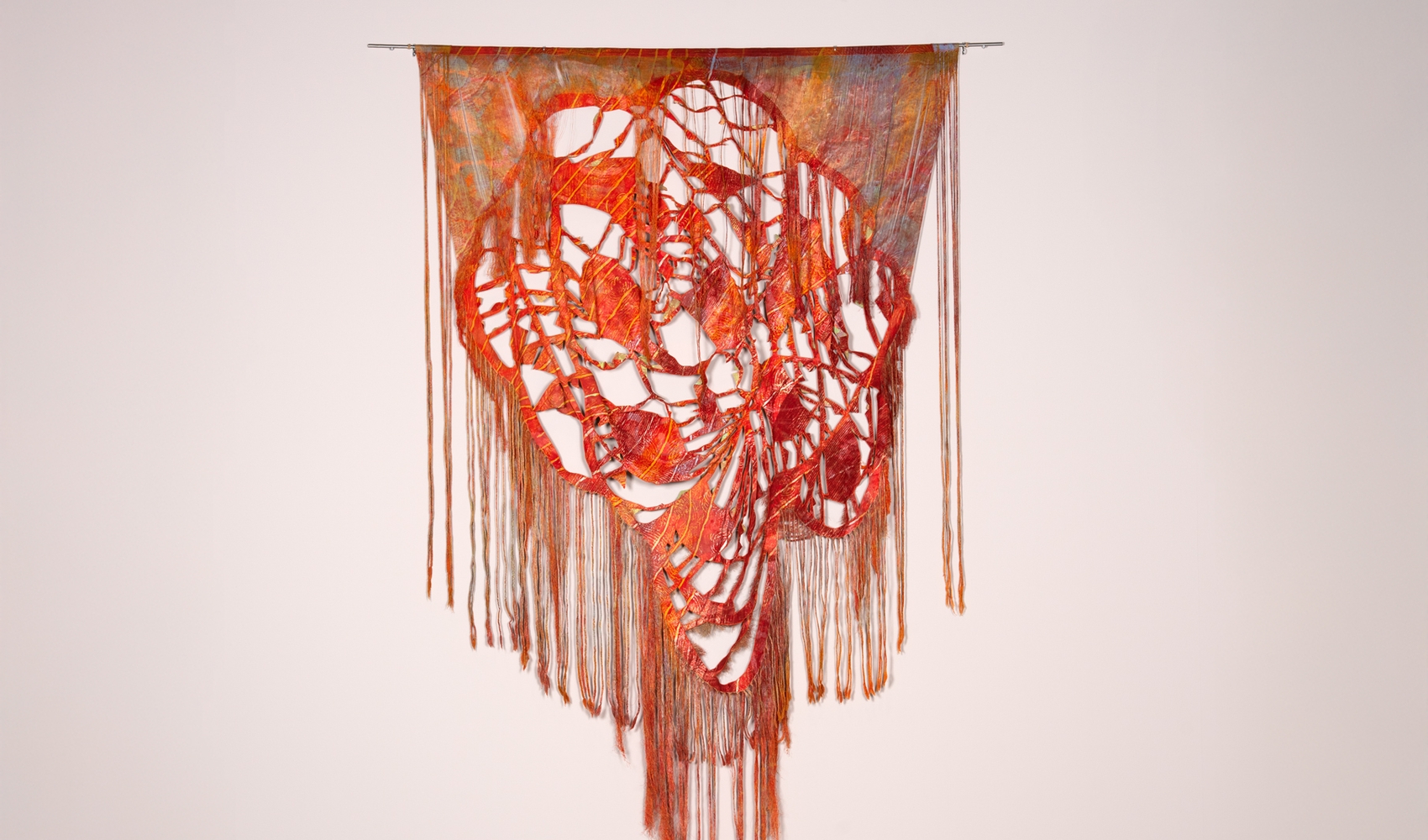 Klippet, sydd, flettet og frynset stofftrykk i røde nyanser, på bomull.