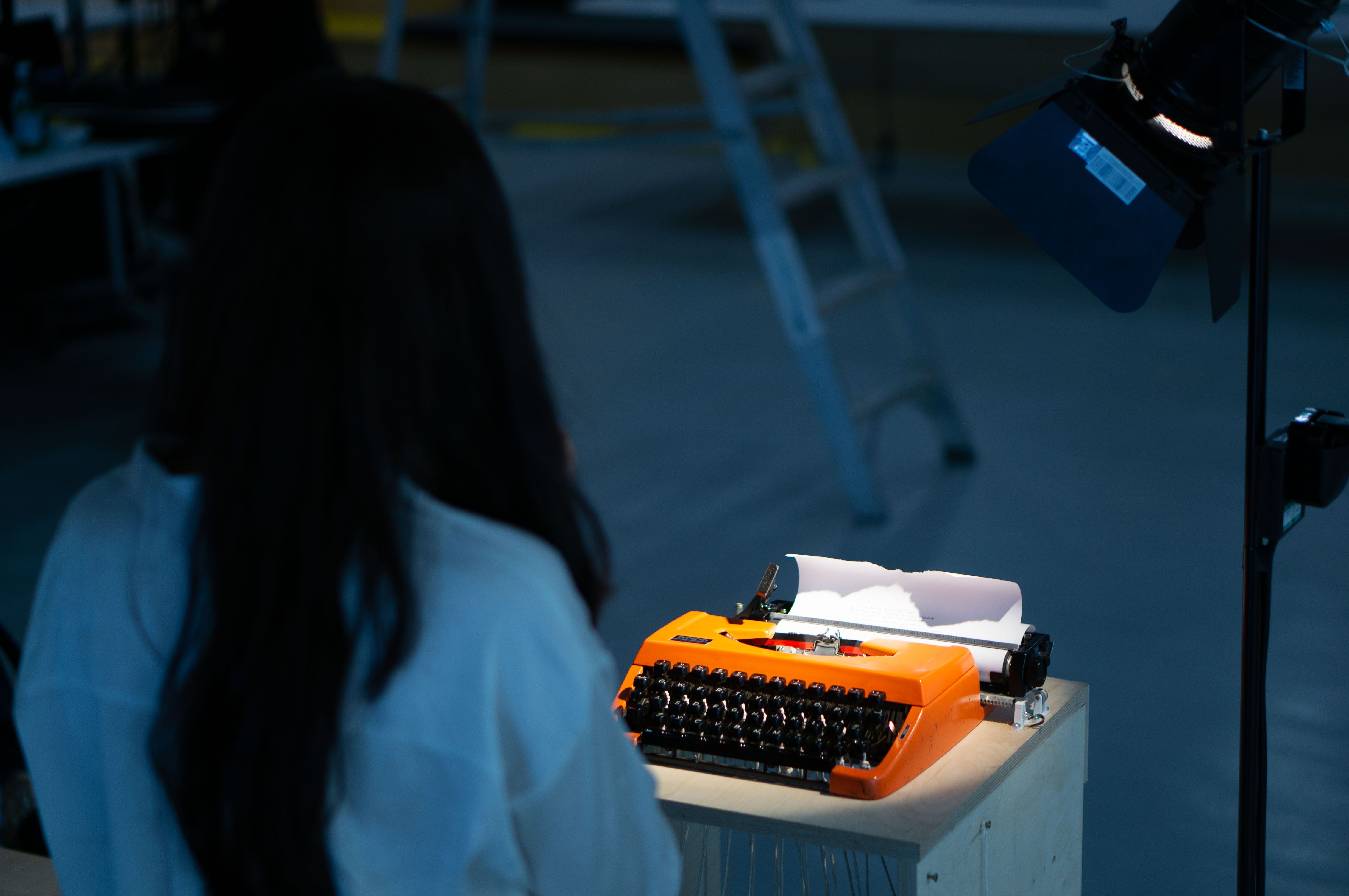 person facing an orange typewriter, with her back to the camera