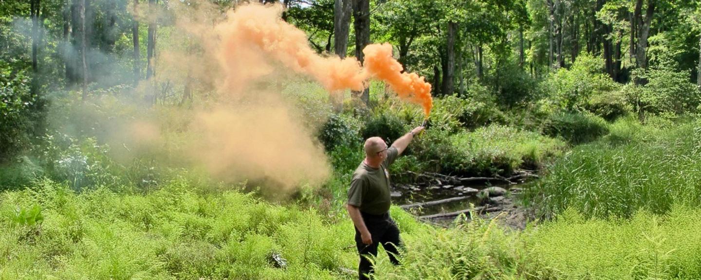 Erik popping orange smoke in front of class in field