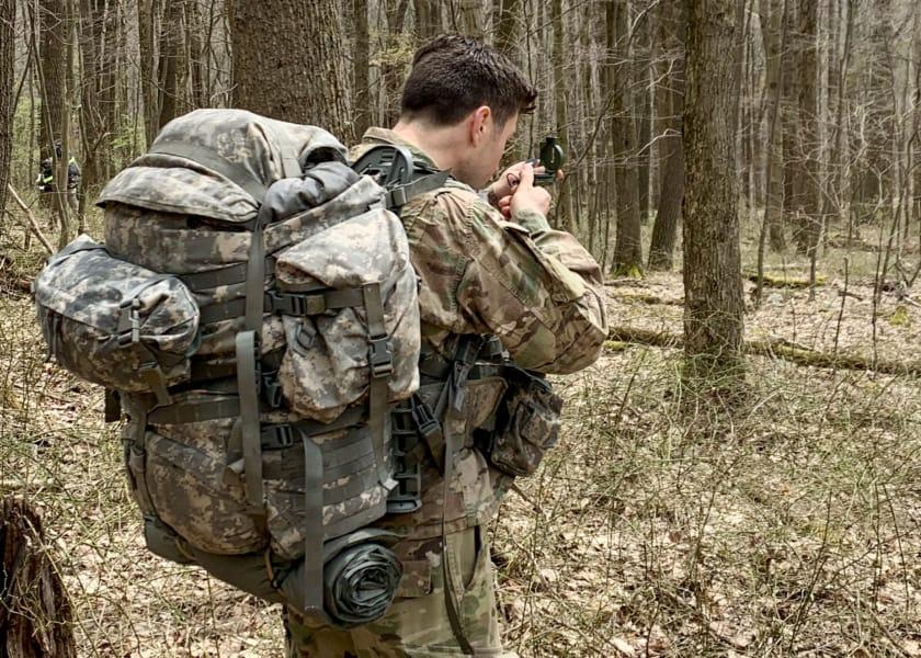 Man in military fatigues looking at compass in forest.