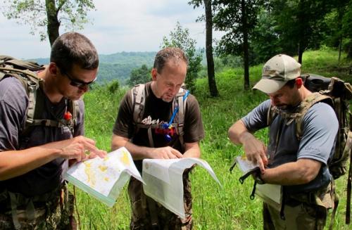 Three men in forest looking at maps