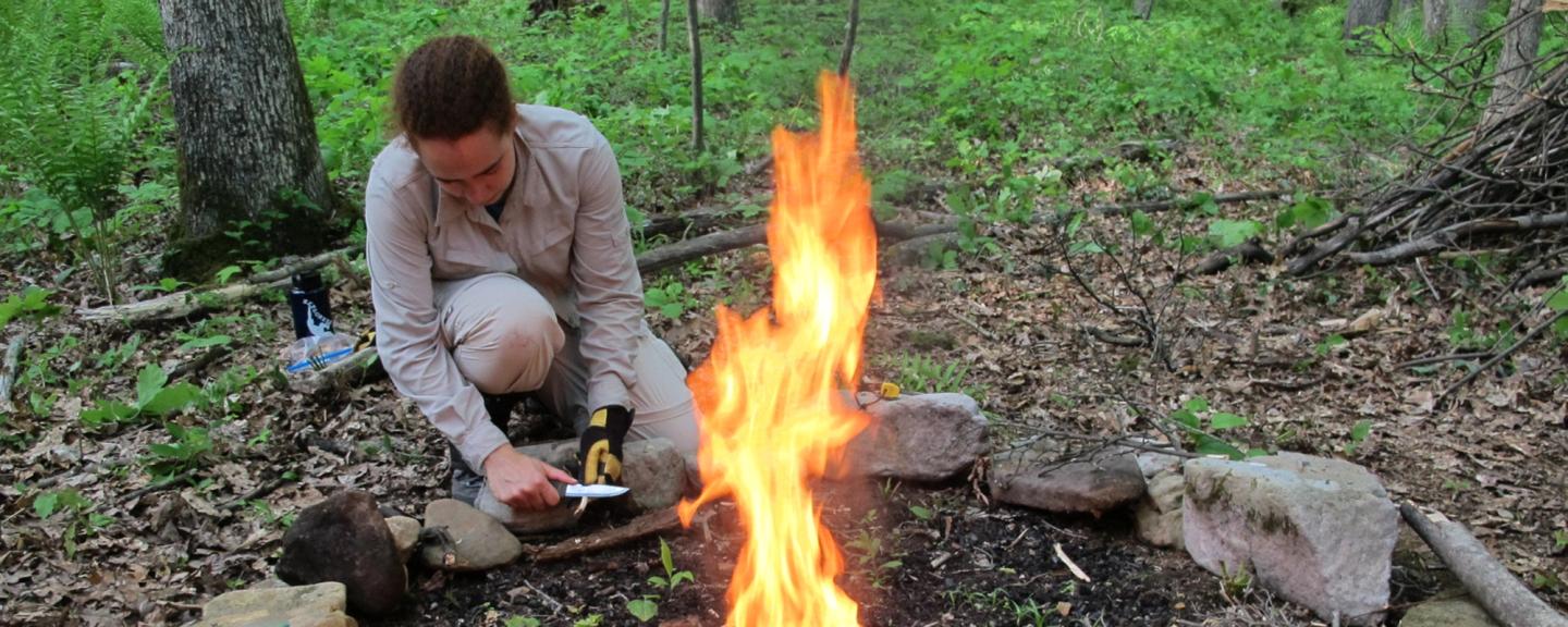 Woman sitting next to fire in forest